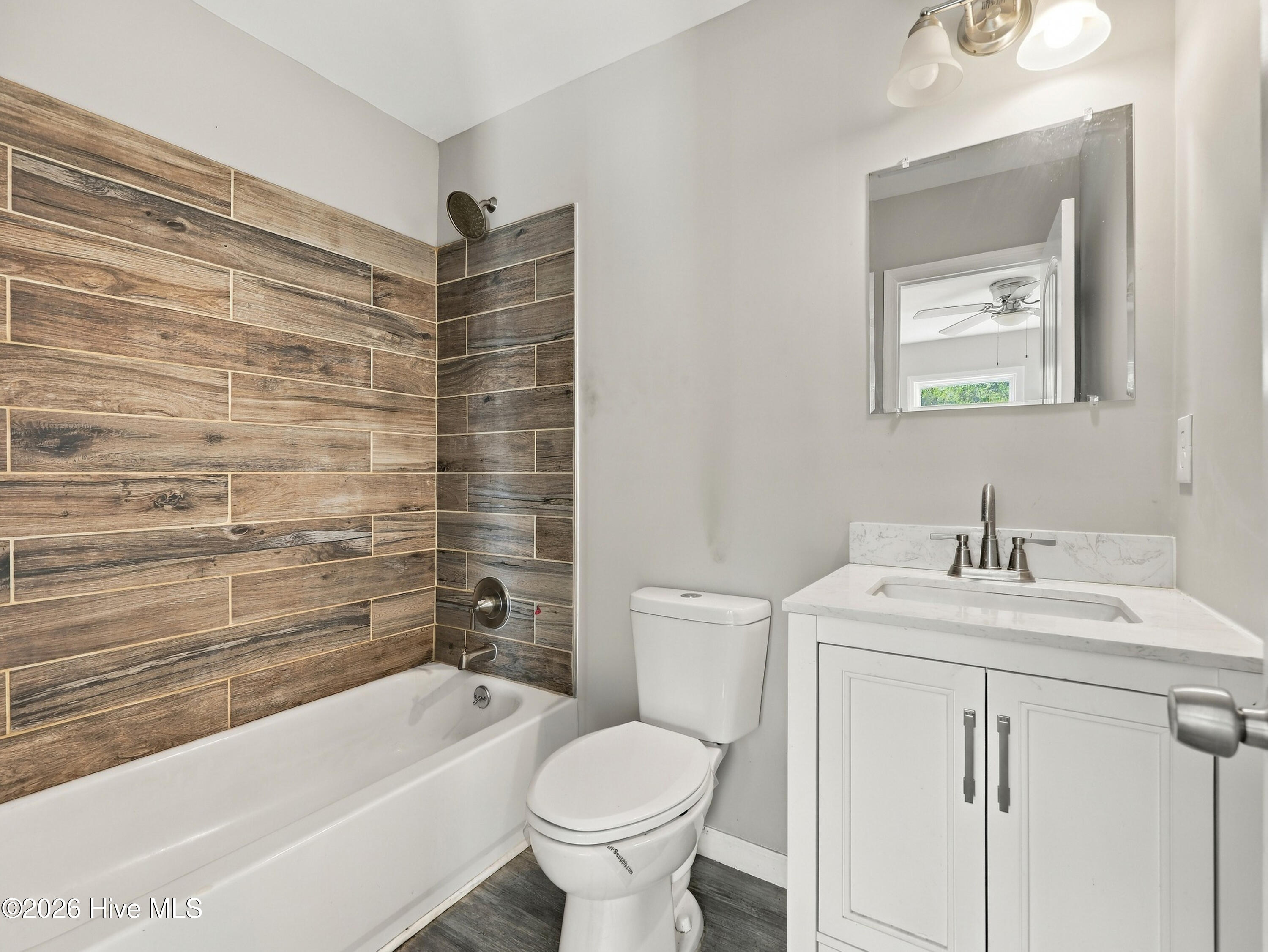 Bathroom with a white vanity and tub, accented by brown wood-look tile around the shower.