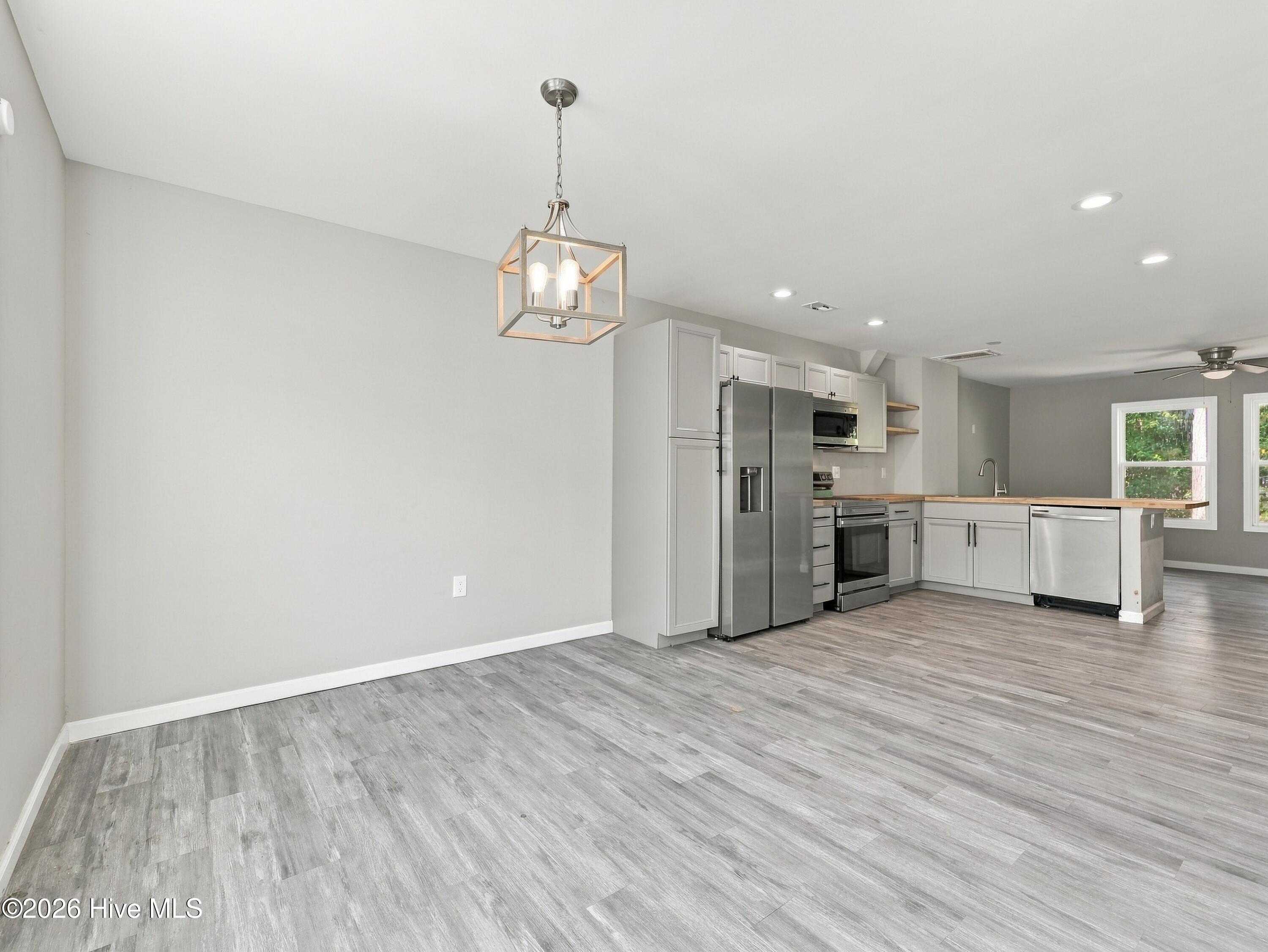 Open kitchen with stainless steel appliances, gray cabinets, and a wood-topped peninsula.