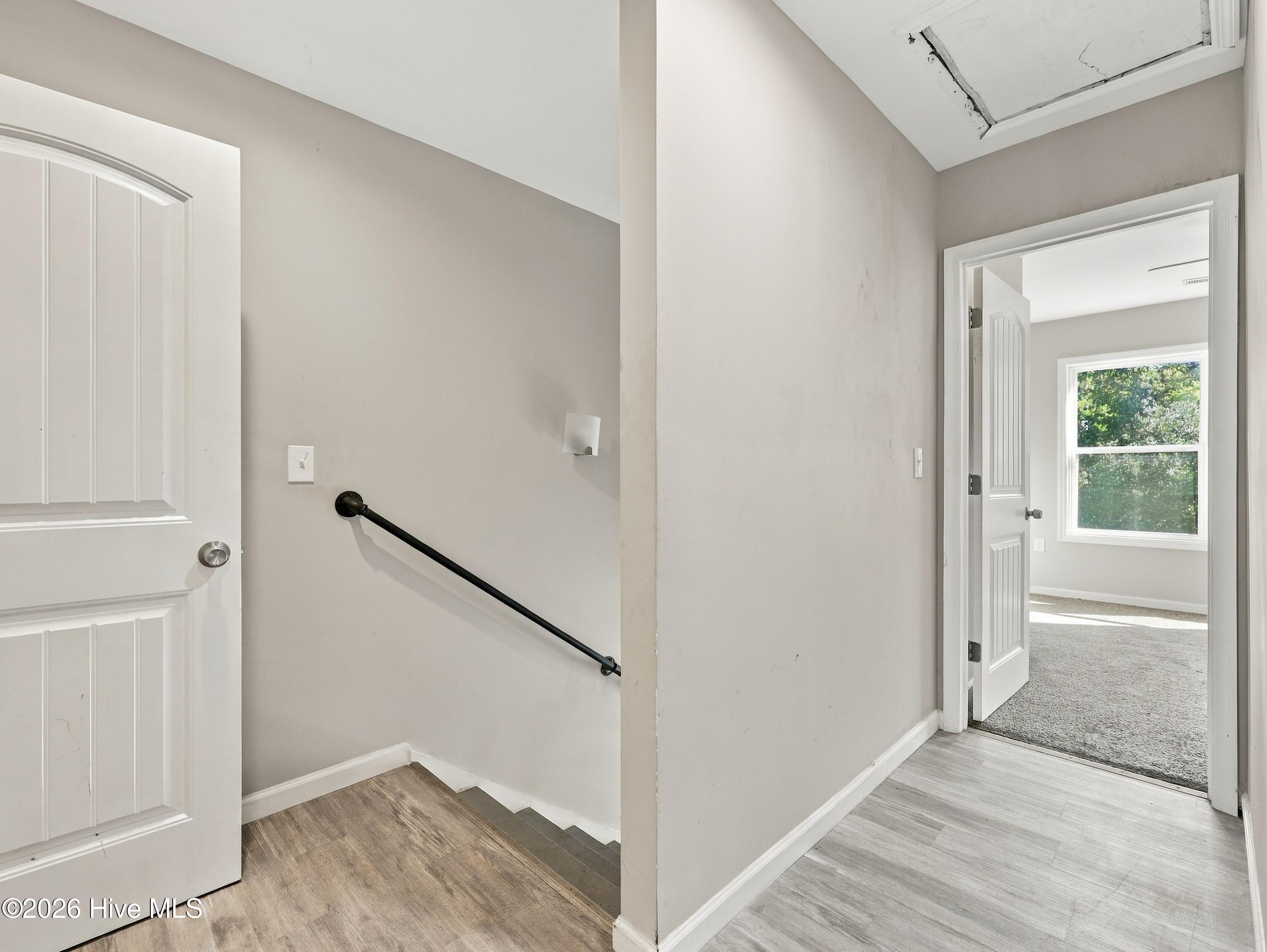 Hallway with stairs, black handrail, and a damaged ceiling panel above an open doorway.