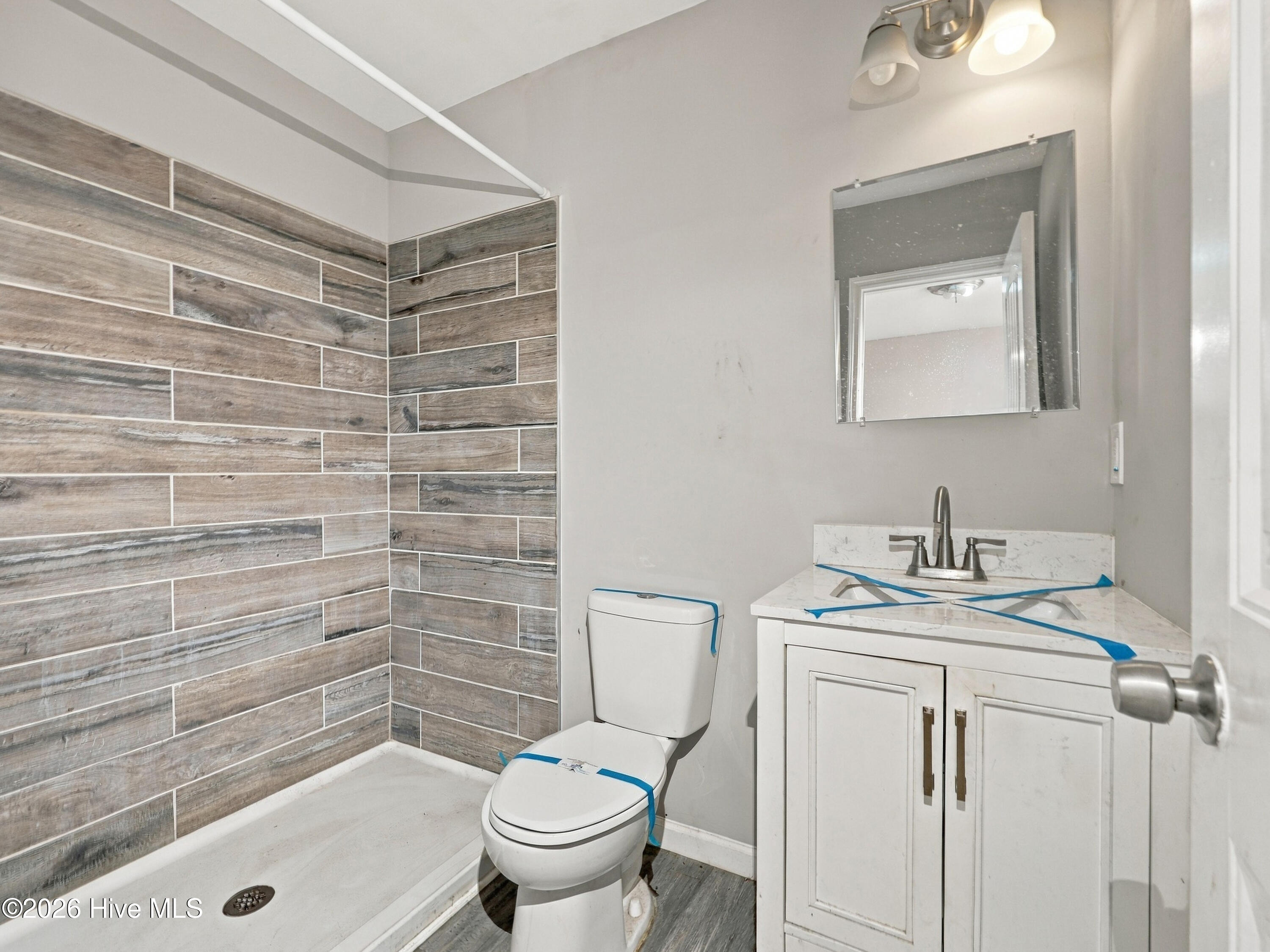 Bathroom with wood-look tiled shower, white toilet, and vanity with marble-look countertop.