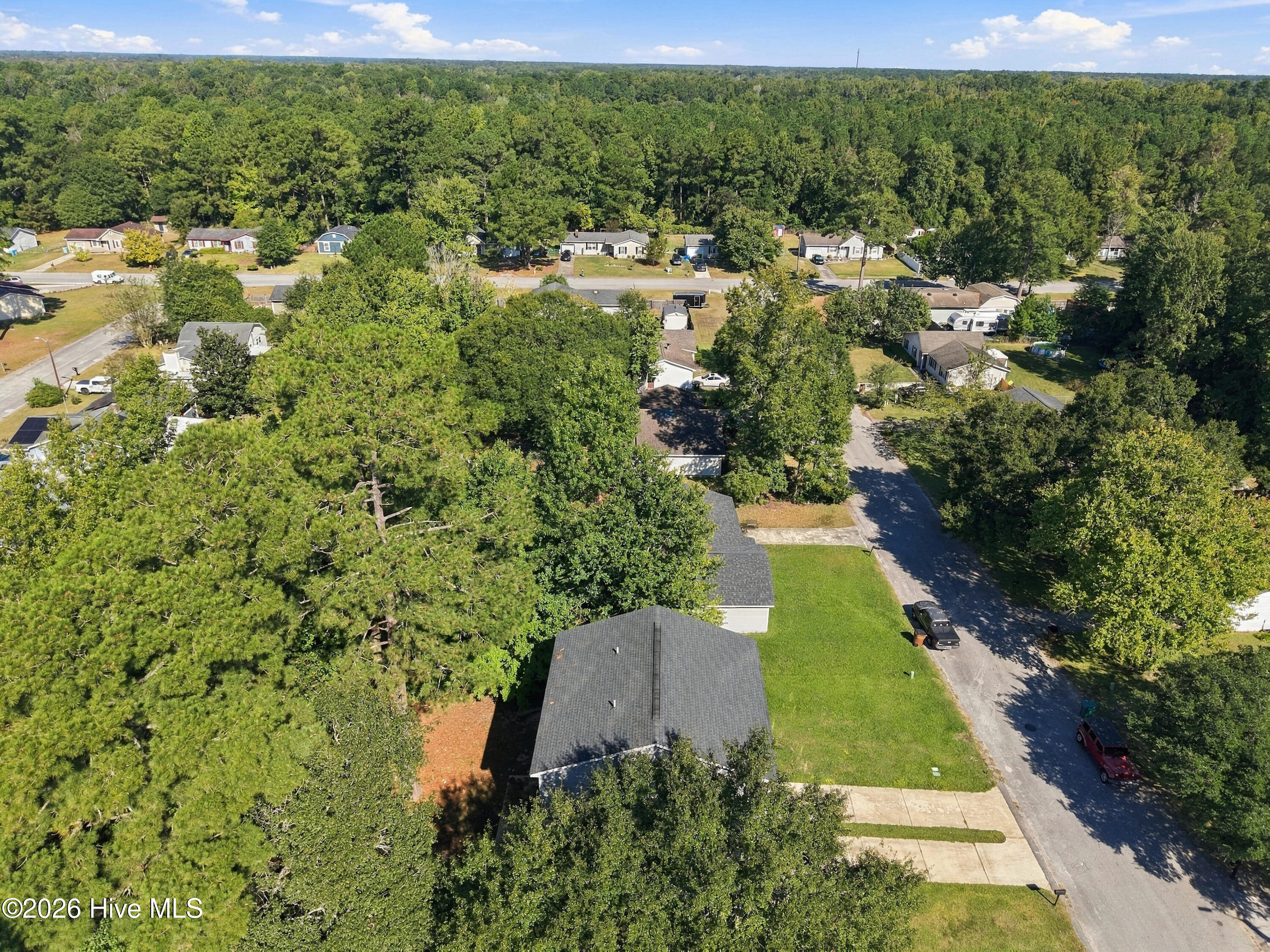 Aerial view of a home with a dark gray roof and lawn beside a tree-lined residential street.