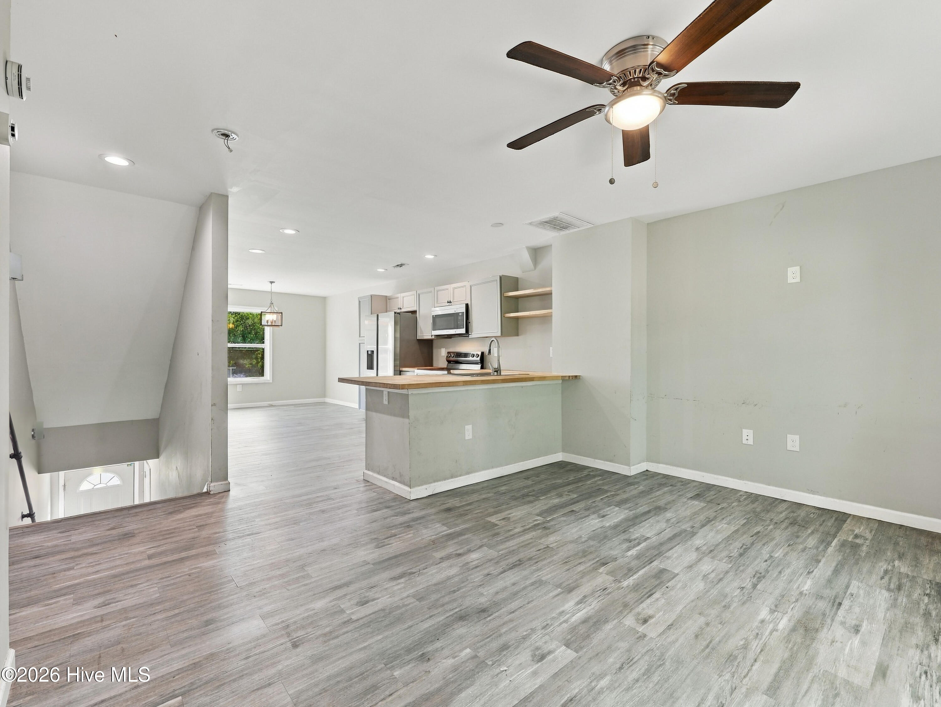 Open living area with gray flooring, ceiling fan, and kitchen island with wood countertop.