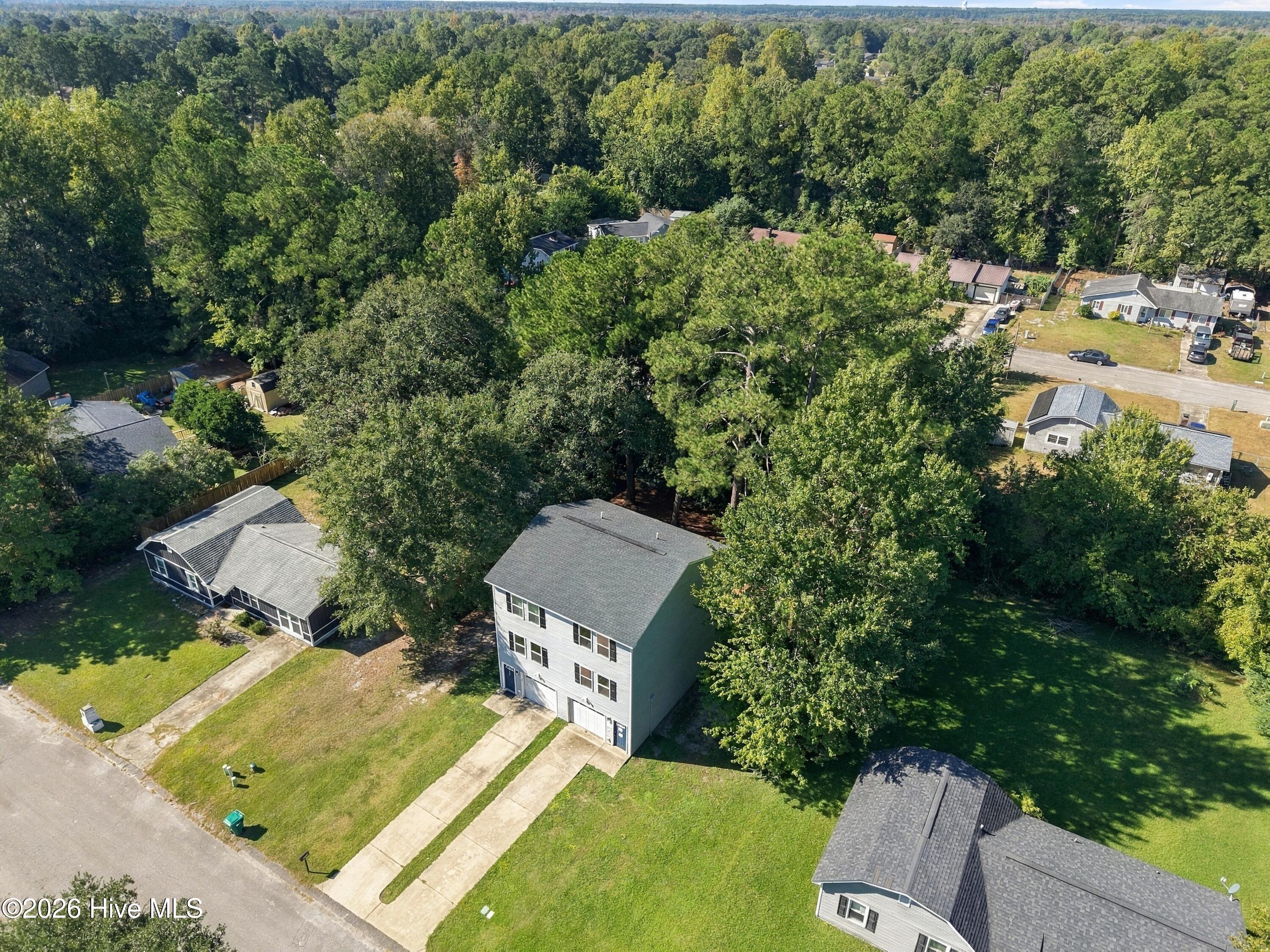 Two-story house on a grassy lot, surrounded by mature trees and neighboring homes.