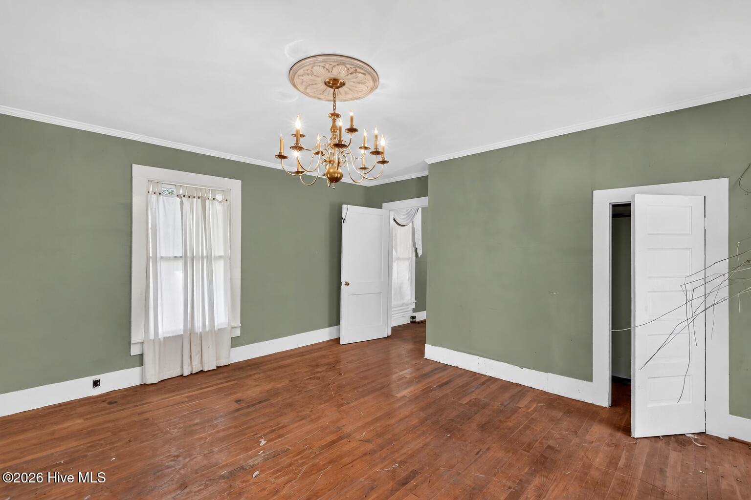 Empty room with sage-green walls, worn hardwood floors, and a brass chandelier.