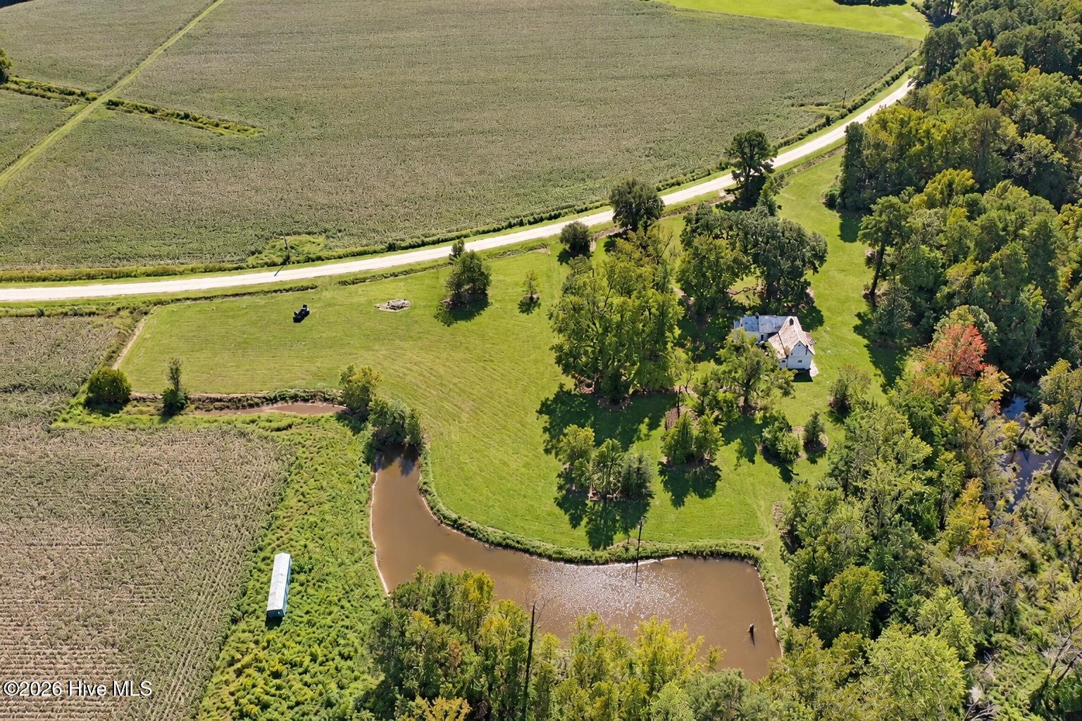 Aerial view of a rural property with a house, pond, open lawn, and surrounding farmland.