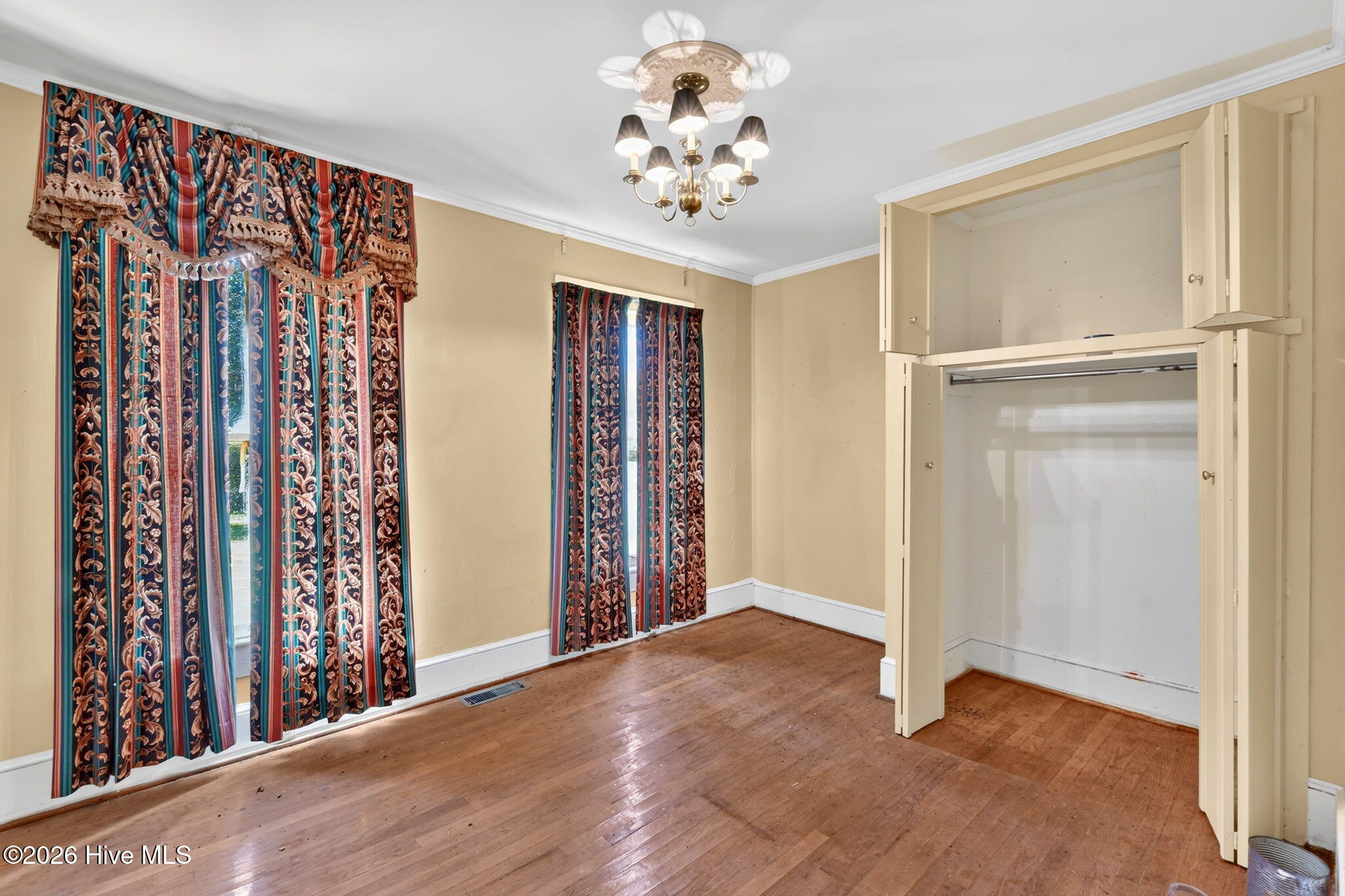 Empty bedroom with hardwood floors, patterned curtains, and a large built-in closet.