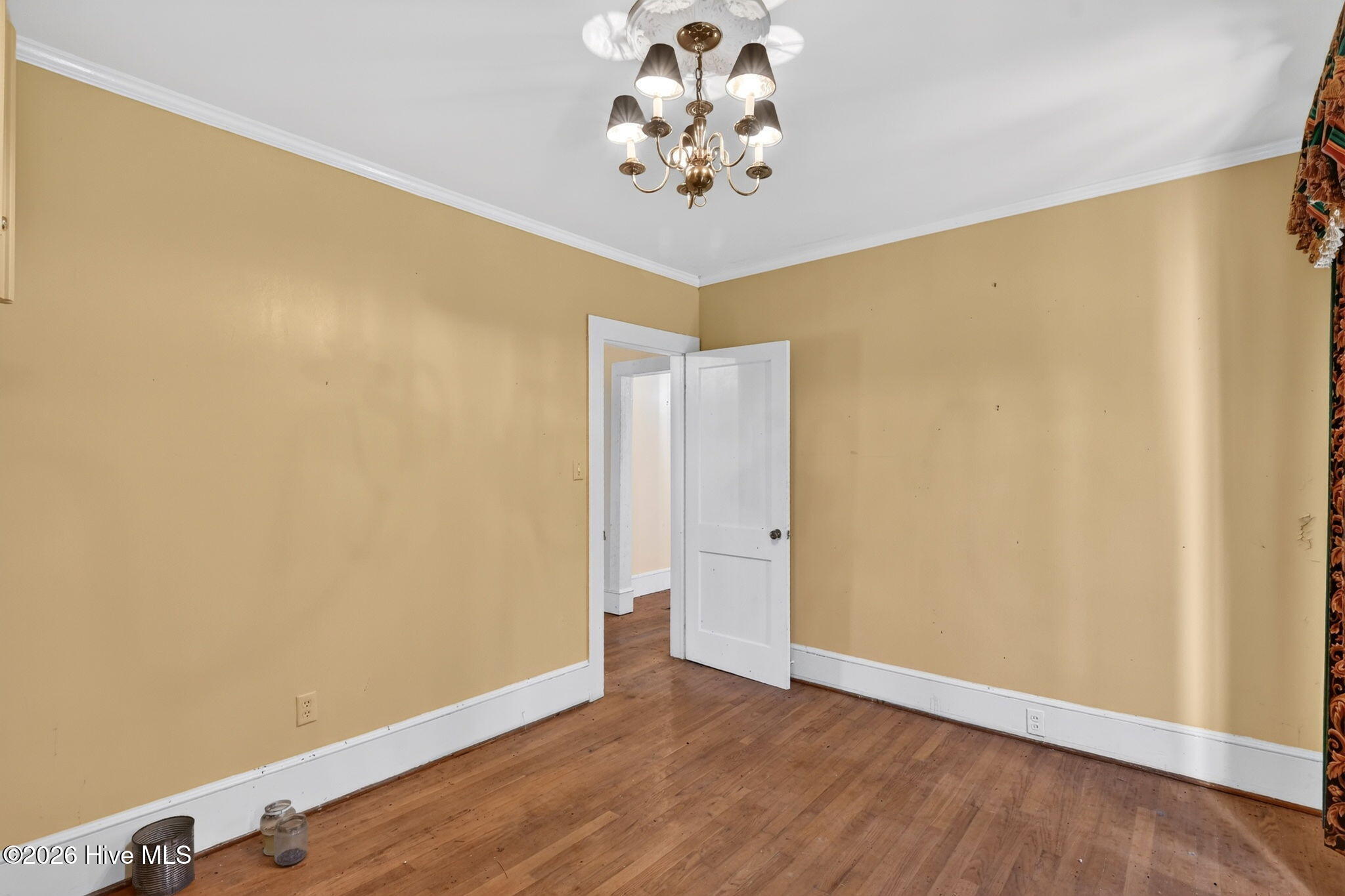 Empty room with mustard-yellow walls, hardwood flooring, and a brass chandelier.