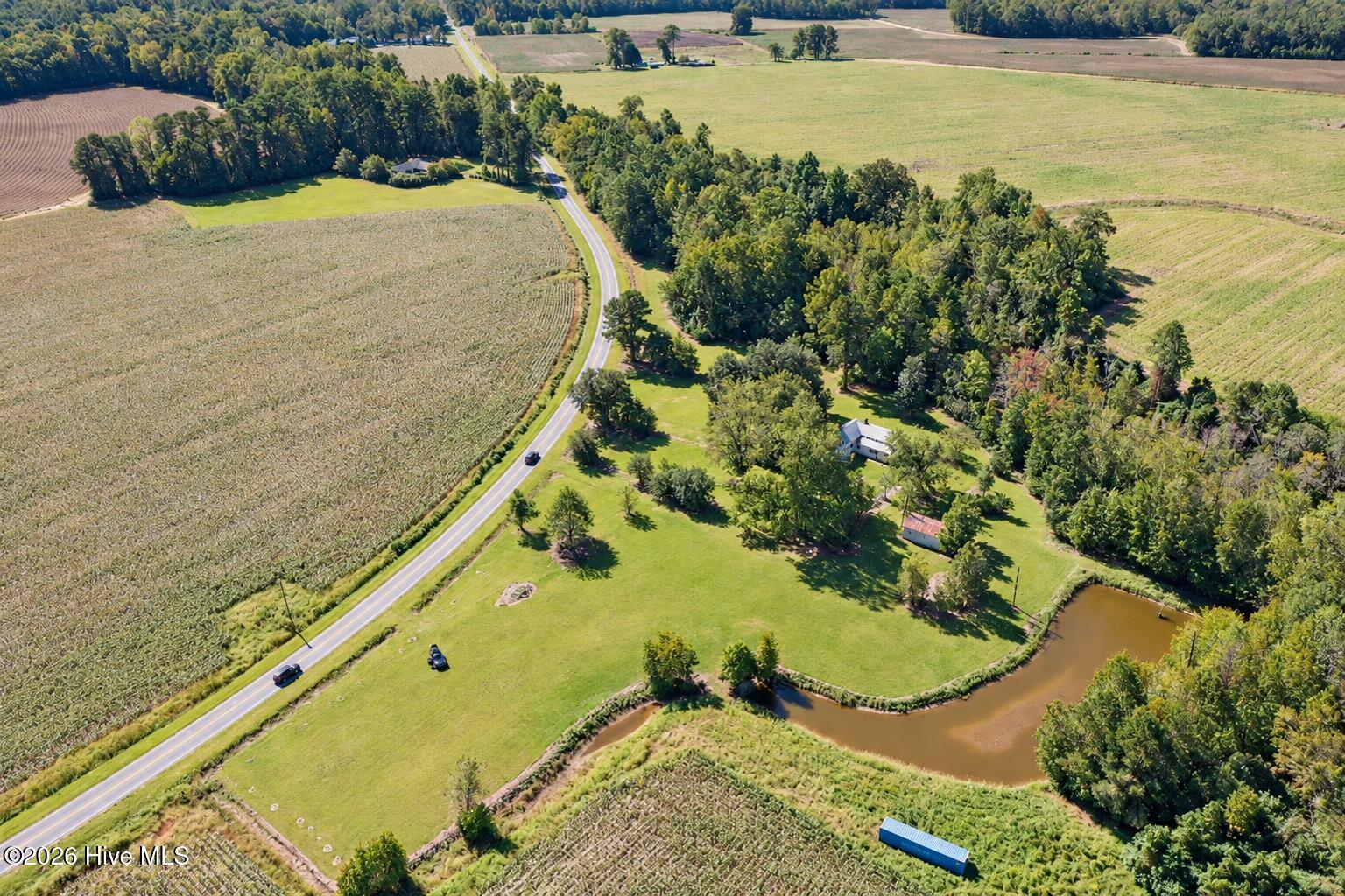 Aerial view of a rural property with a house, surrounding farmland, and a pond beside the road.