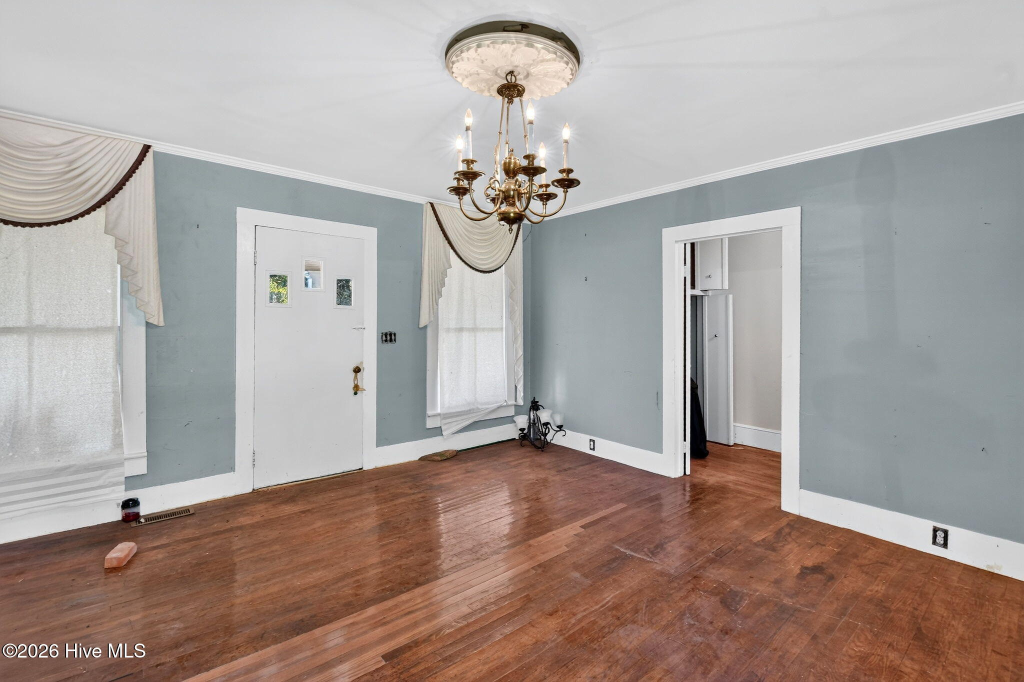Empty dining room with blue-gray walls, hardwood floors, and a brass chandelier.