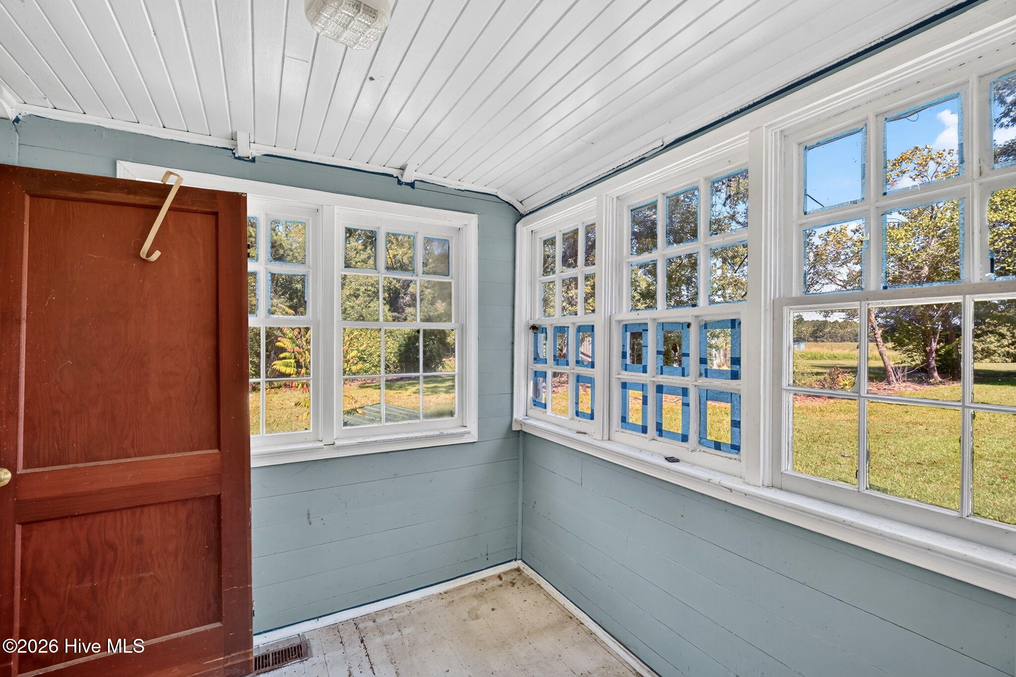 Enclosed porch with pale blue walls, a white paneled ceiling, and many windows overlooking an autumn yard.