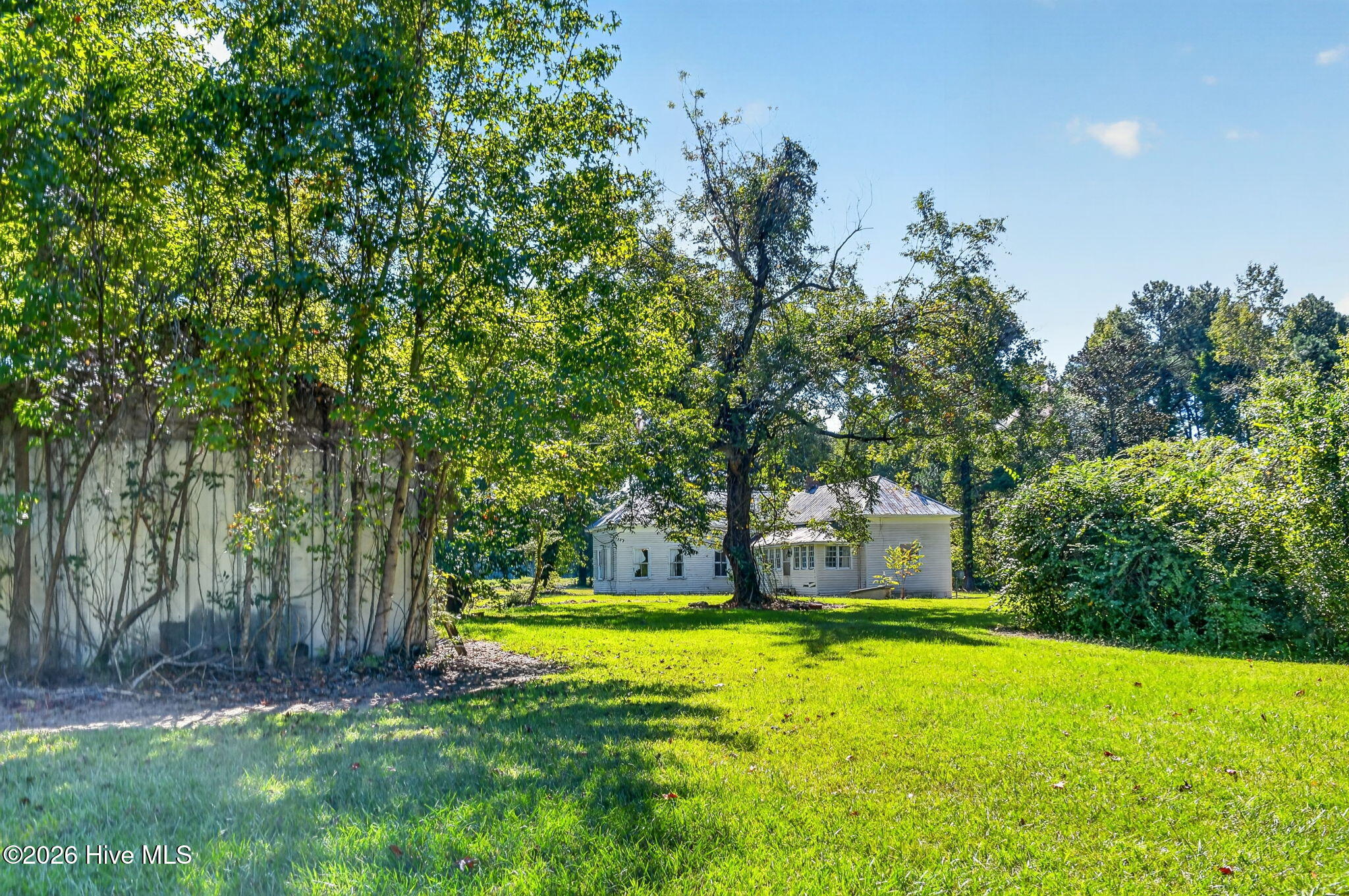 White single-story house with a metal roof, set behind a lawn and mature trees.