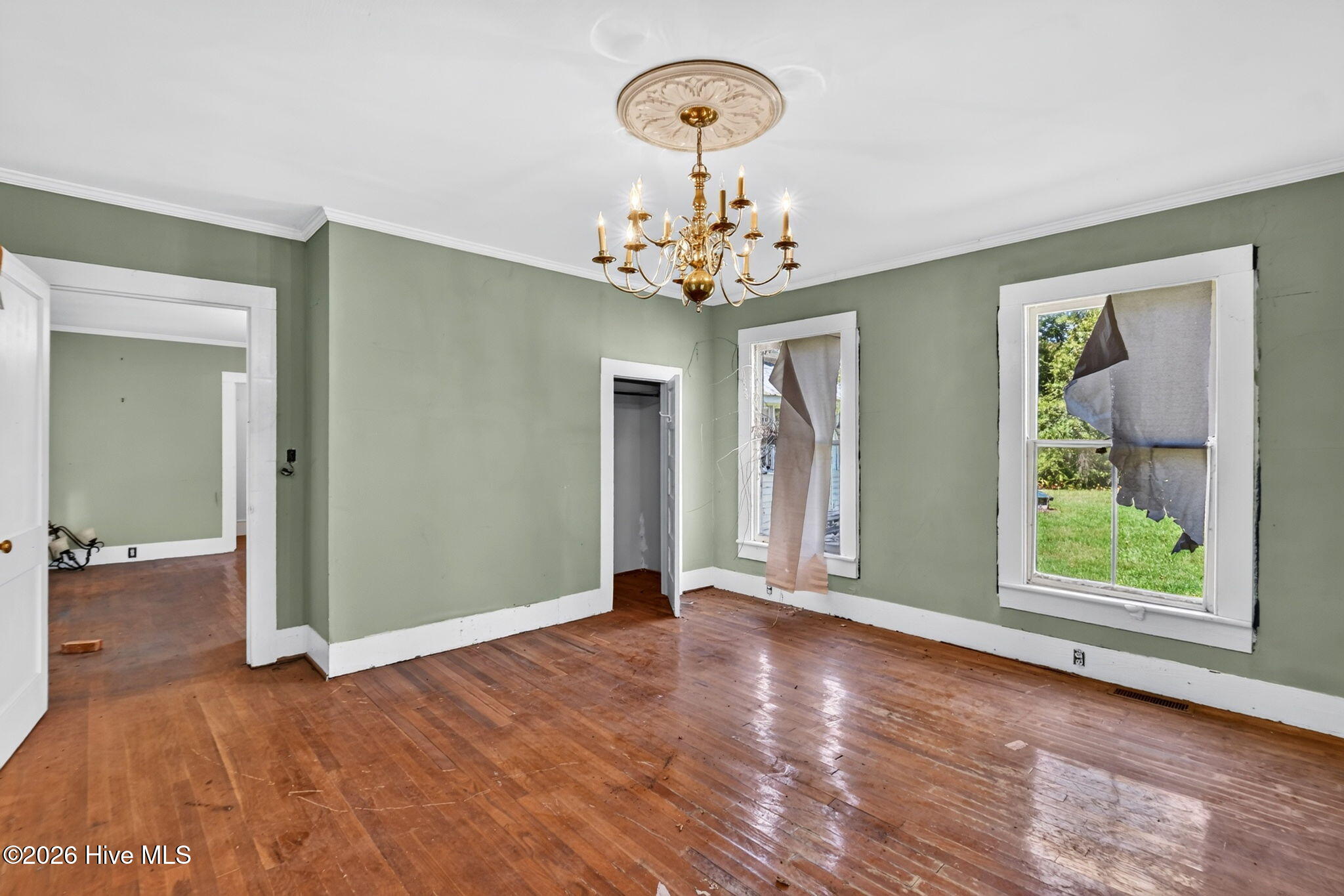 Empty room with a brass chandelier, sage-green walls, and worn hardwood floors.