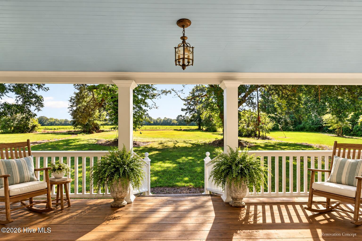 Covered porch with rocking chairs and potted ferns overlooking a broad green lawn.