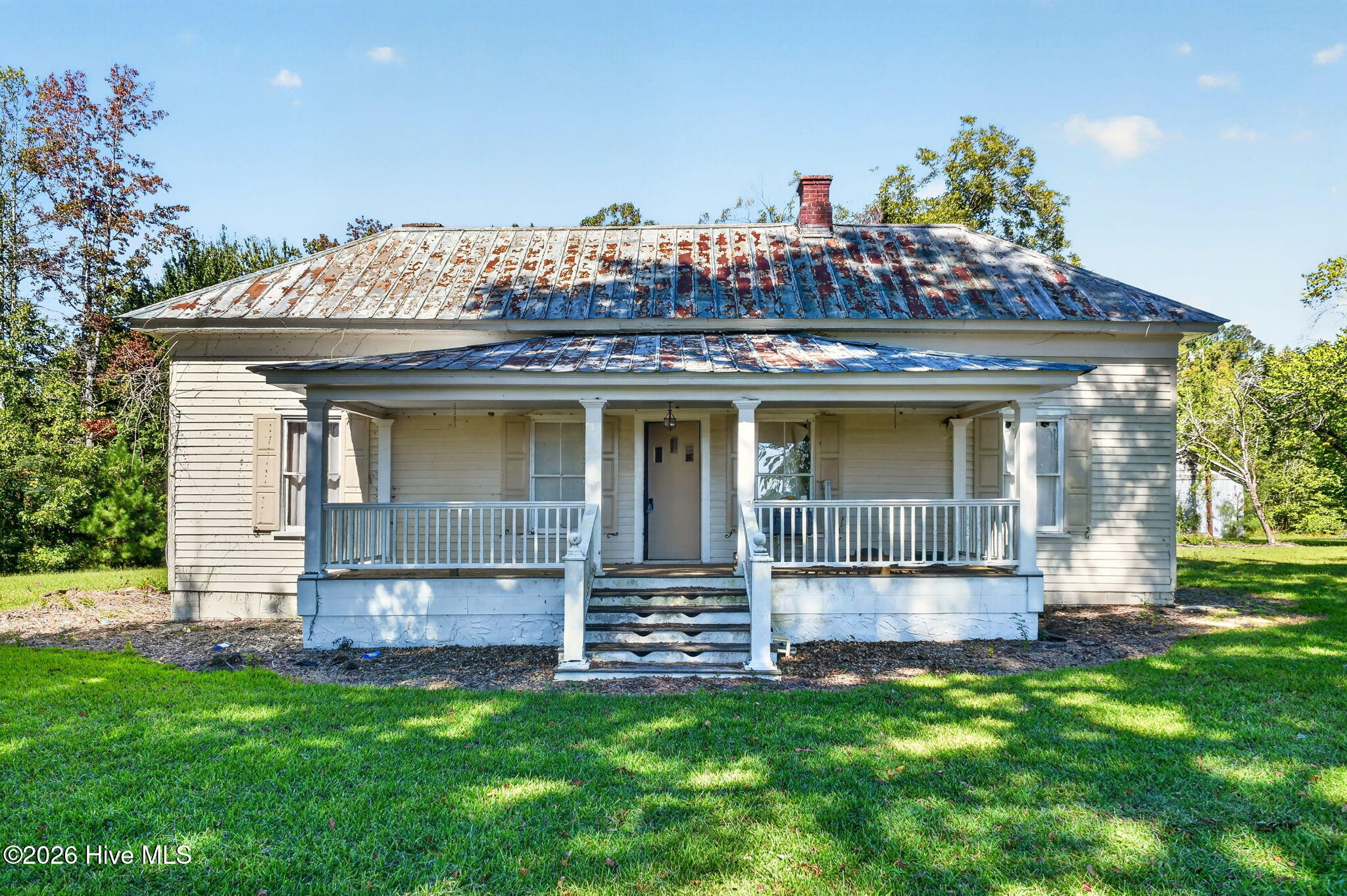 Single-story house with a covered front porch, white railings, and a weathered metal roof.