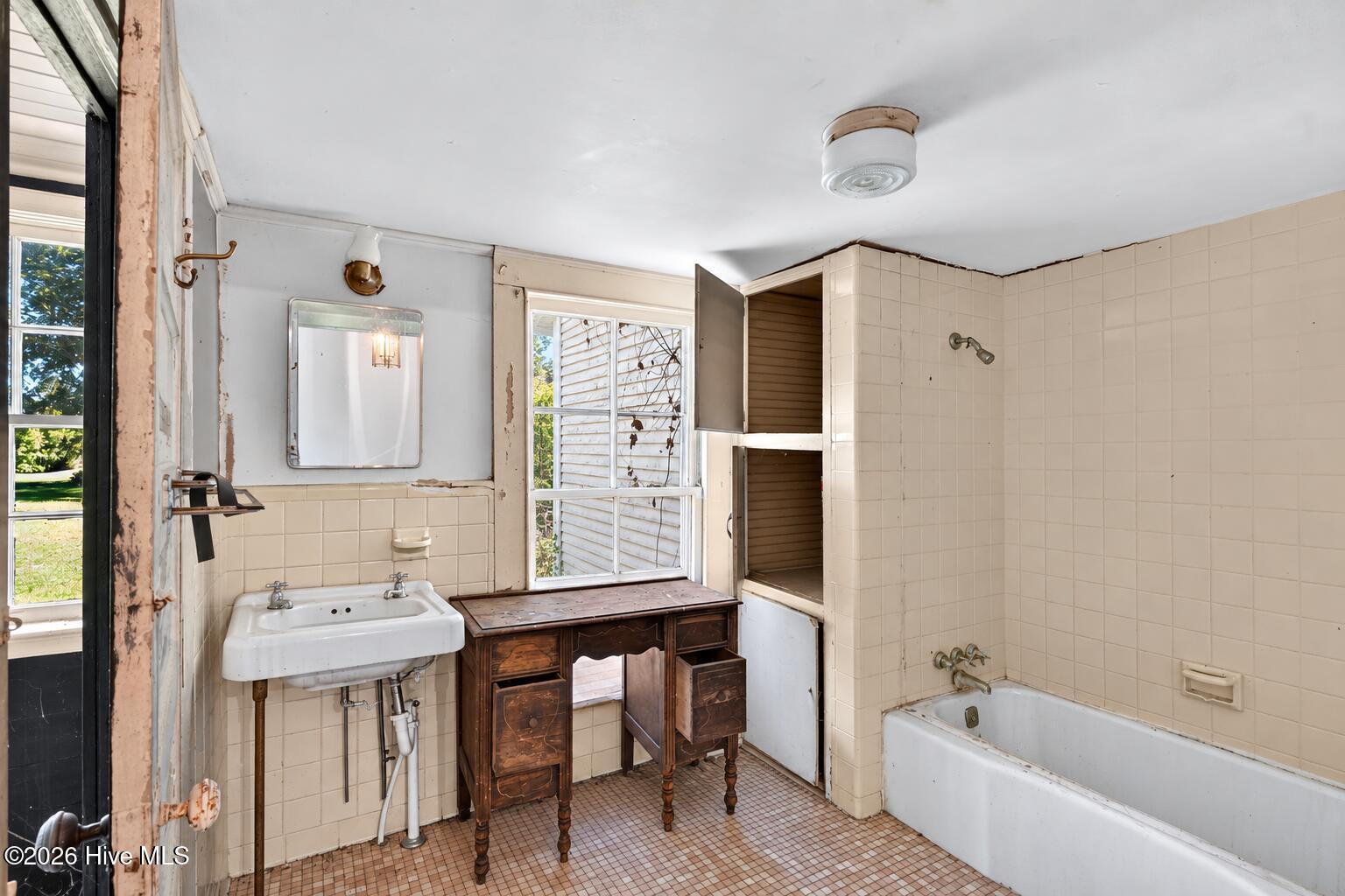 Dated tiled bathroom with a white tub, wall-mounted sink, and dark wooden vanity.