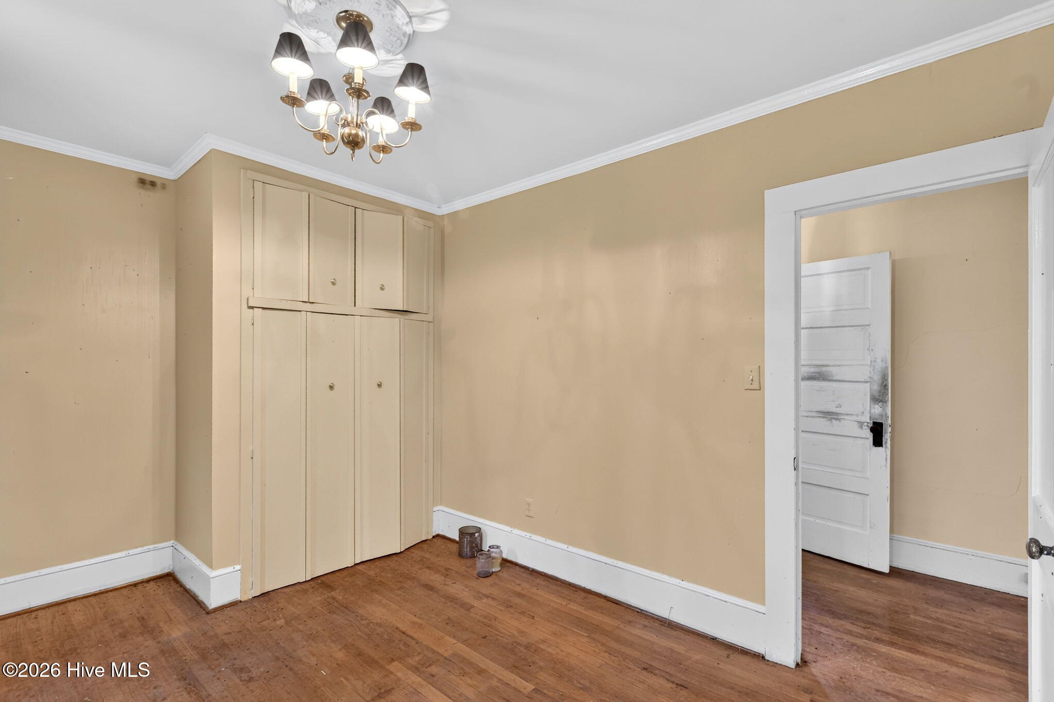 Empty room with a built-in cupboard, hardwood floors, and a chandelier.
