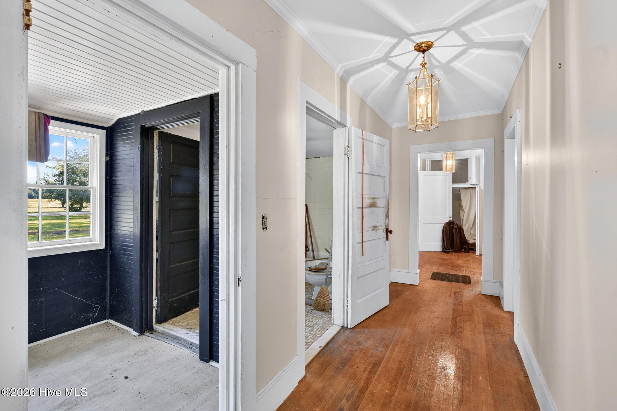 Hallway with worn hardwood floors, a brass pendant light, and open doorways to adjoining rooms.