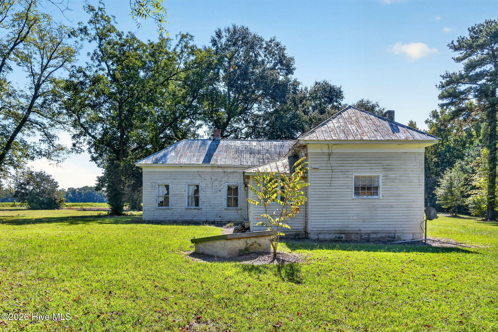 White house with weathered siding and metal roofs on a tree-lined lawn.