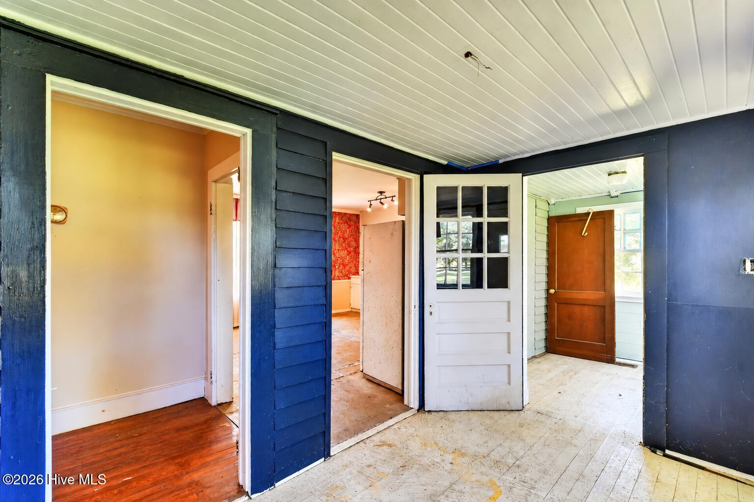 Covered entryway with dark blue siding, worn flooring, and several doorways.