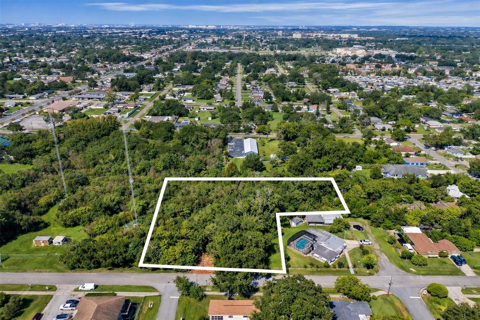 Aerial view of a wooded vacant lot outlined in white beside homes and a swimming pool.