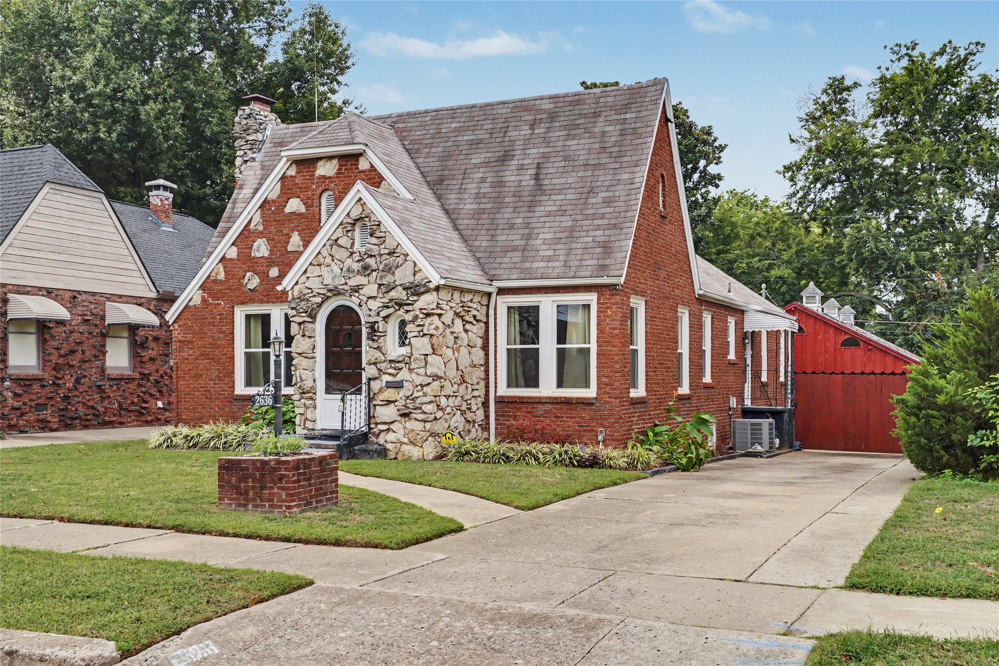 Red-brick home with a stone-fronted arched entry and red garage beside the driveway.