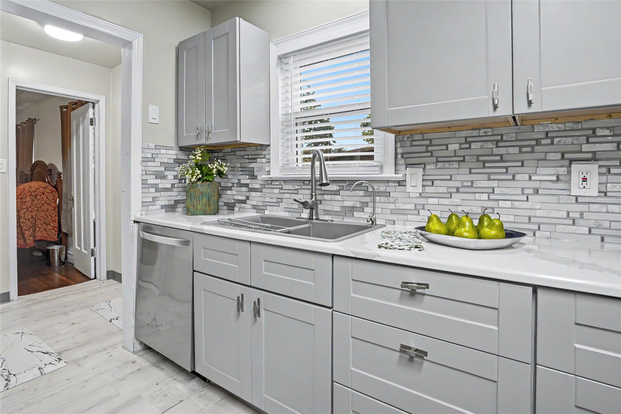 Bright kitchen with white cabinetry, a geometric tile backsplash, and a stainless steel sink beneath a window.