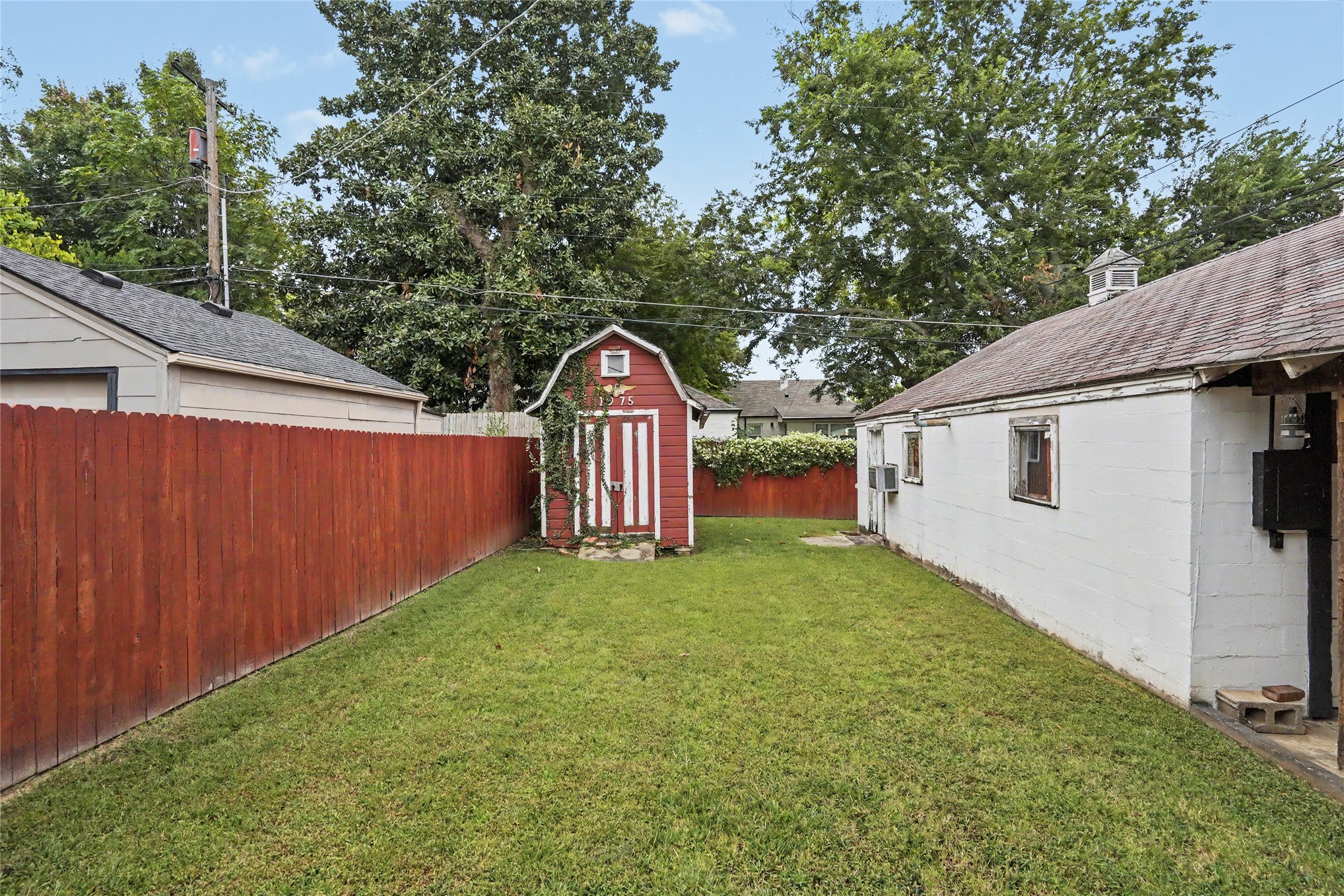 Grassy backyard with a red privacy fence, a small red shed, and white outbuildings.