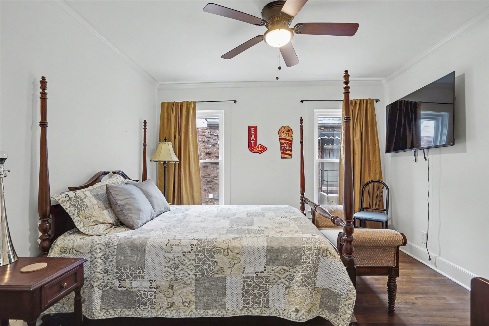 Bedroom with a four-poster bed, patterned quilt, gold curtains, and wall-mounted television.