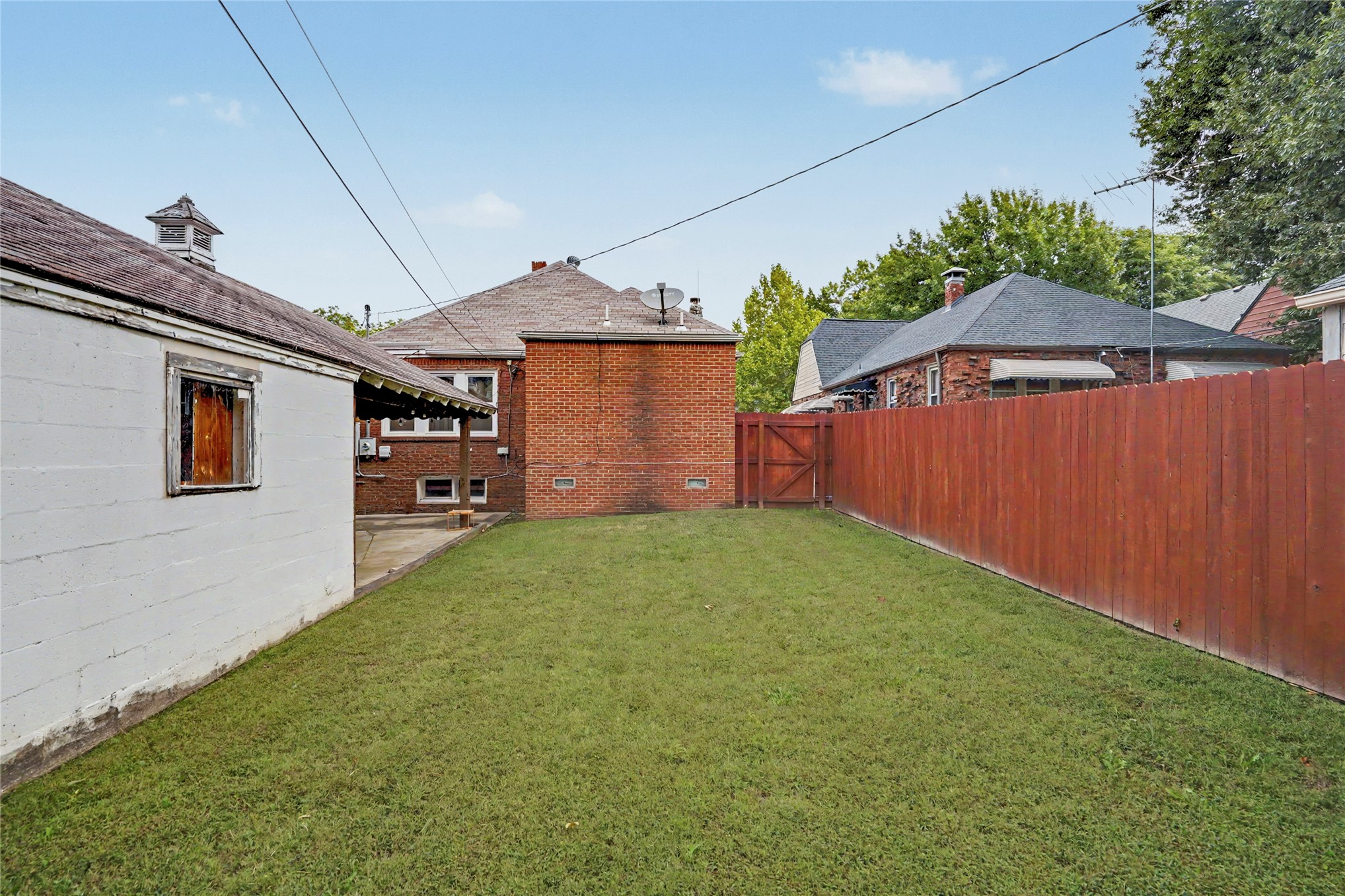 Backyard with a broad lawn, red privacy fence, and brick house.