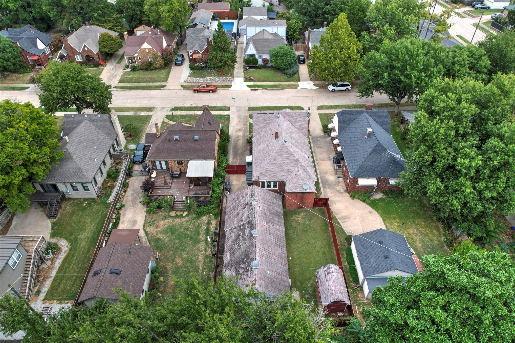 Aerial view of a brick house, backyard, and neighboring homes along a tree-lined street.