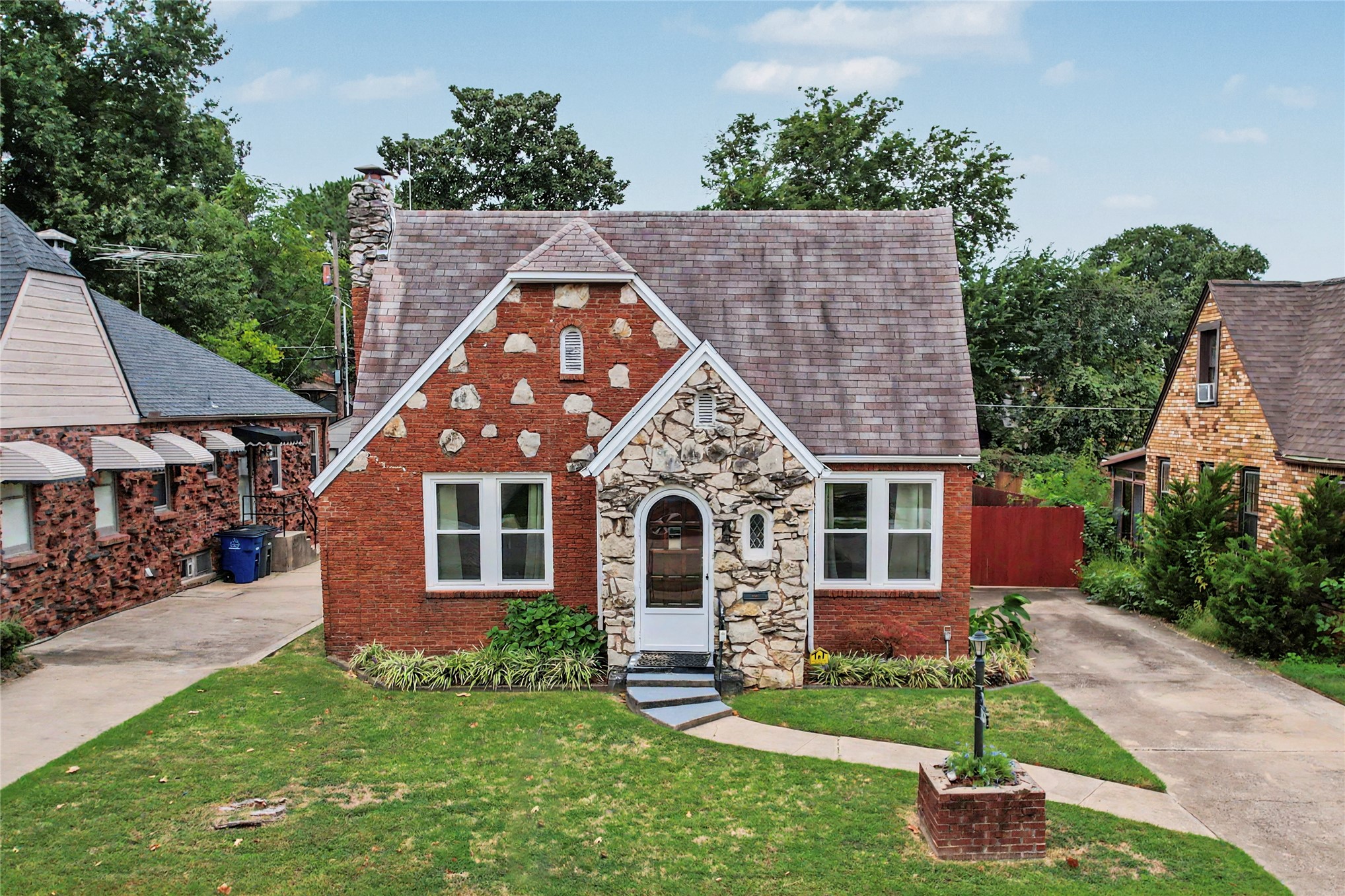 Brick and stone home with a steep roof, arched entry, and front lawn.