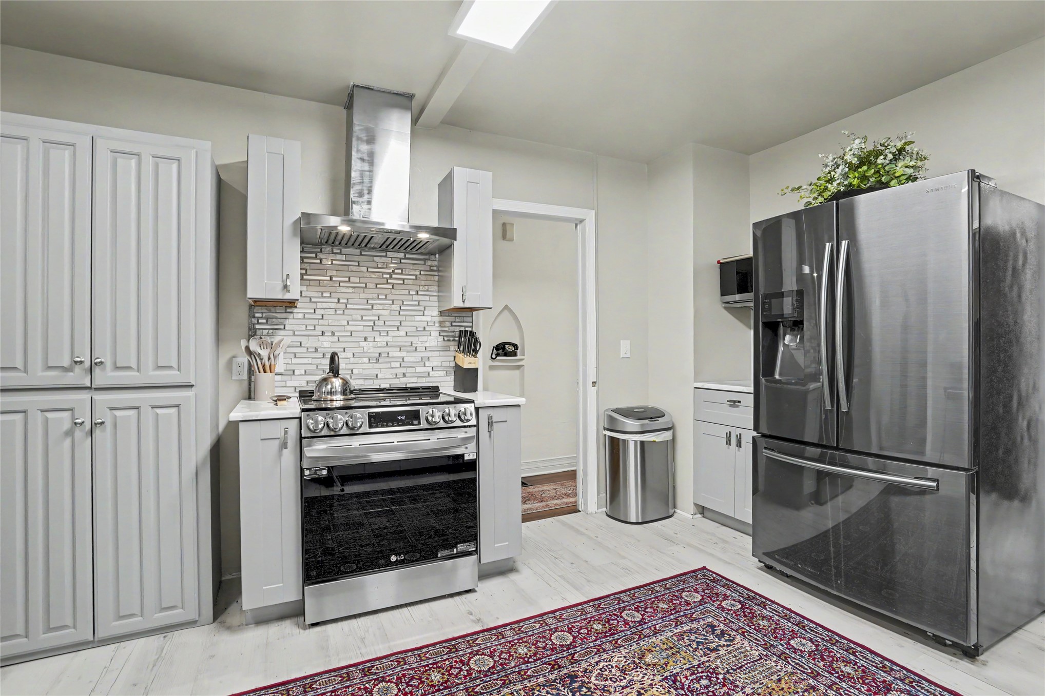 Kitchen with white cabinets, stainless appliances, a tiled backsplash, and a patterned red rug.