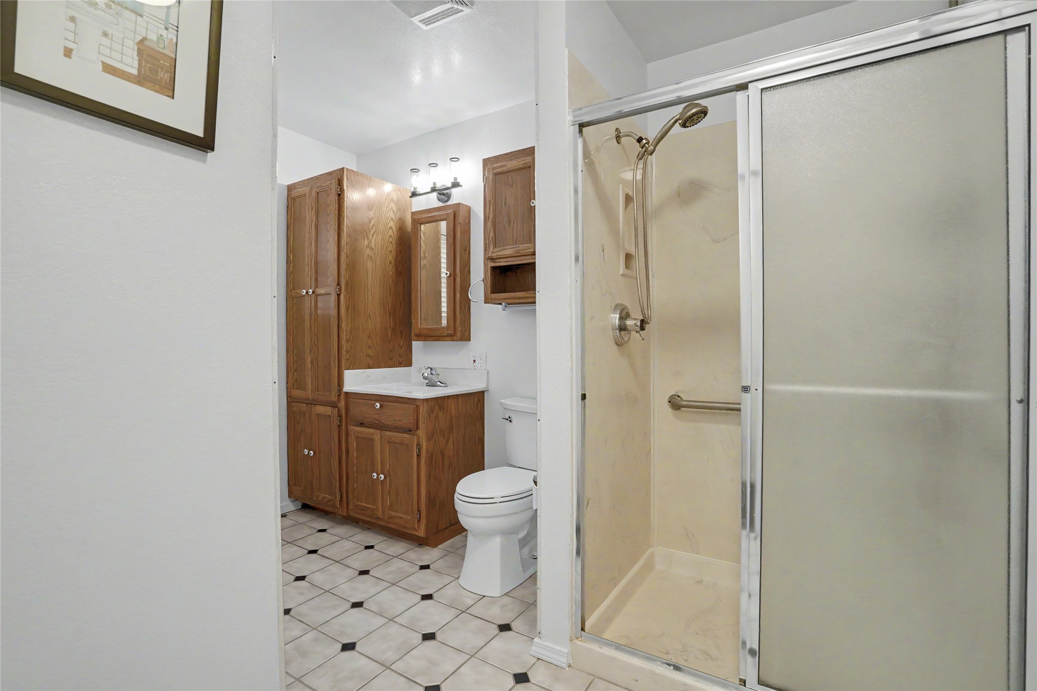 Bathroom with a glass shower, wood cabinets, and a light tiled floor with dark accents.