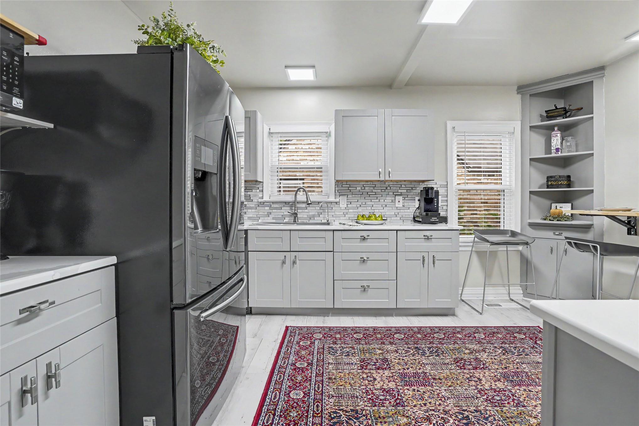 Kitchen with white cabinets, tiled backsplash, stainless steel refrigerator, and a red patterned rug.