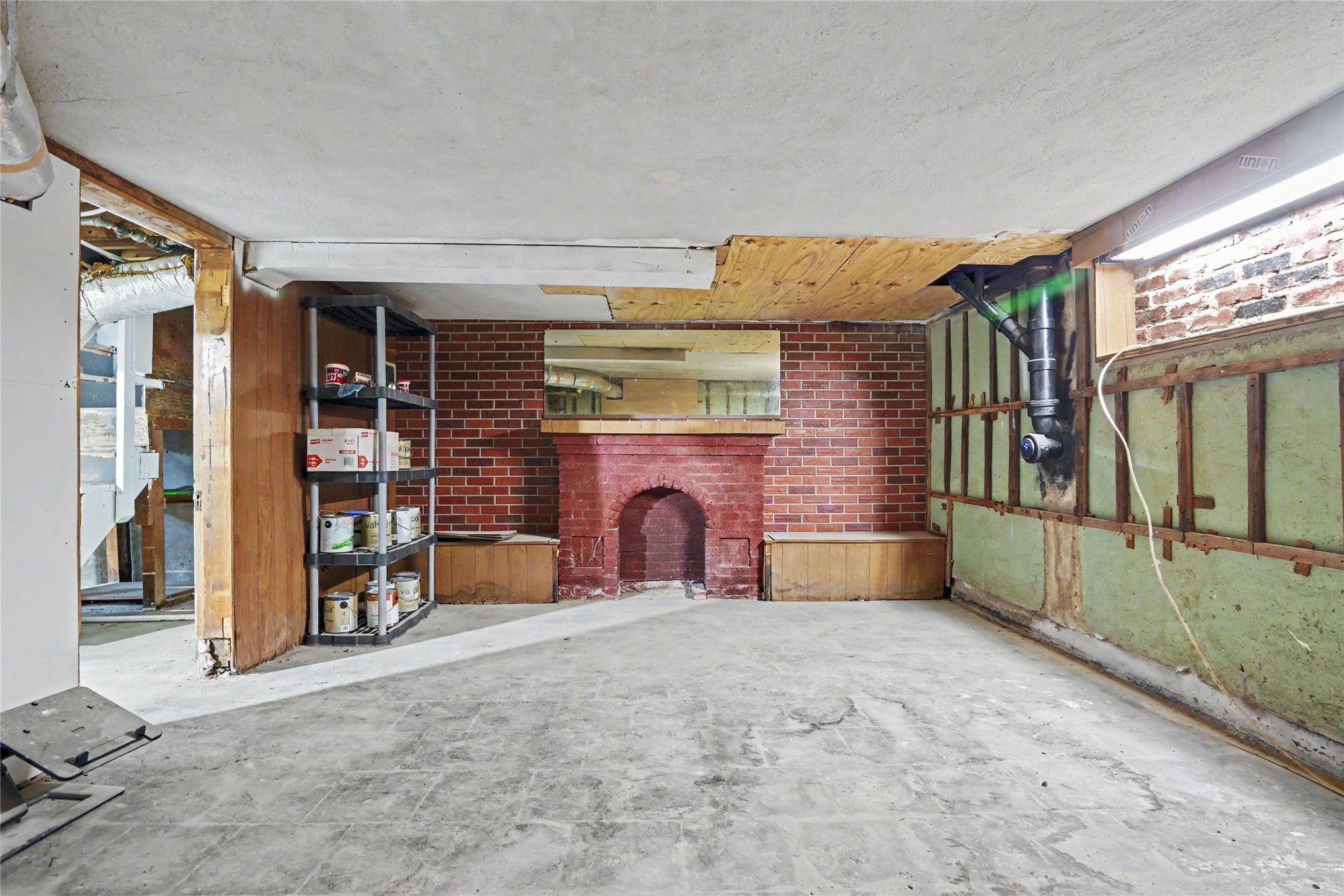 Unfinished basement with a brick fireplace, exposed framing, and a concrete floor.