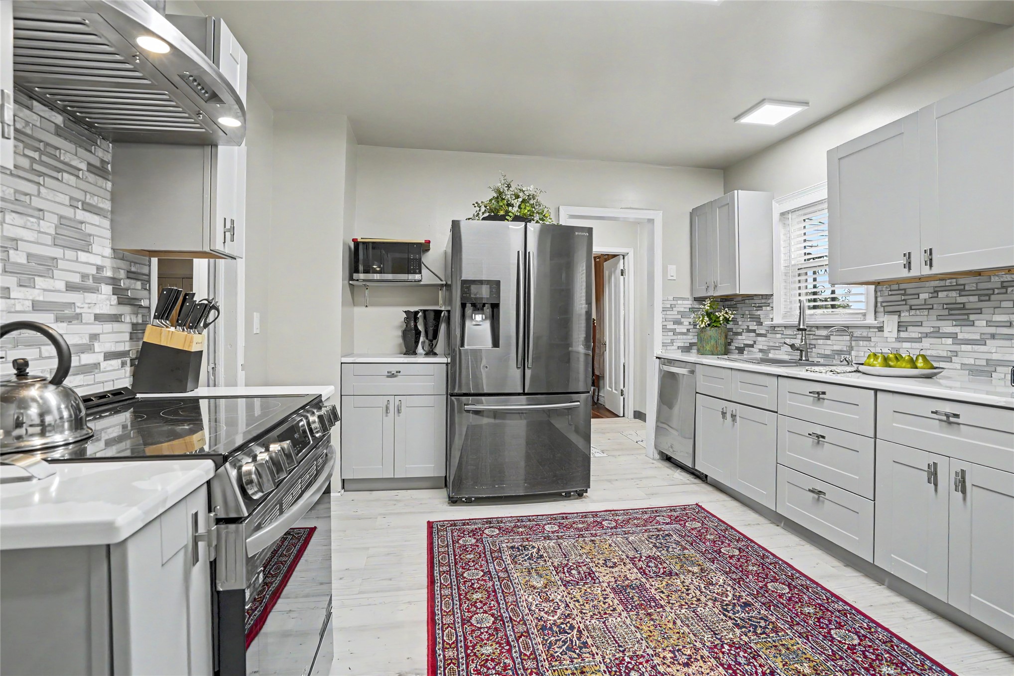 Kitchen with white cabinetry, stainless steel appliances, patterned tile backsplash, and a red area rug.