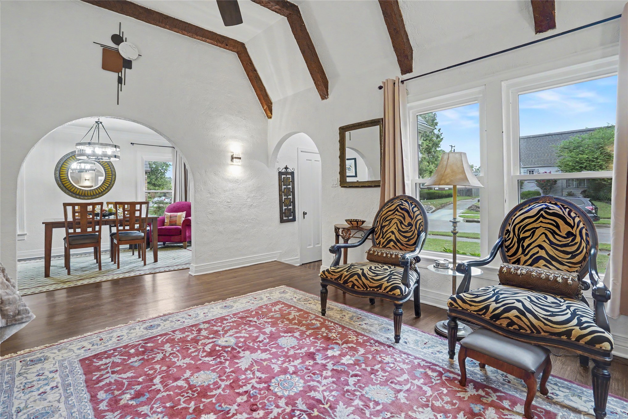 Living room with exposed ceiling beams, arched openings, and patterned armchairs by tall windows.