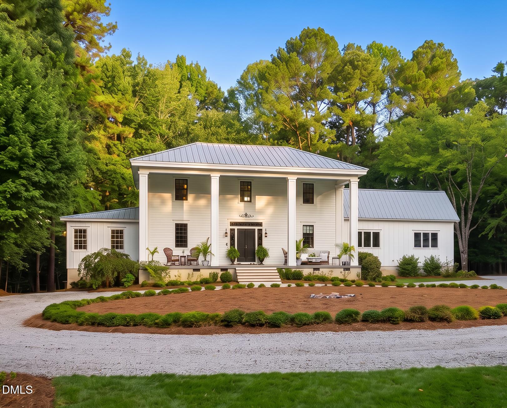 White two-story house with a metal roof, broad covered porch, and mature trees.