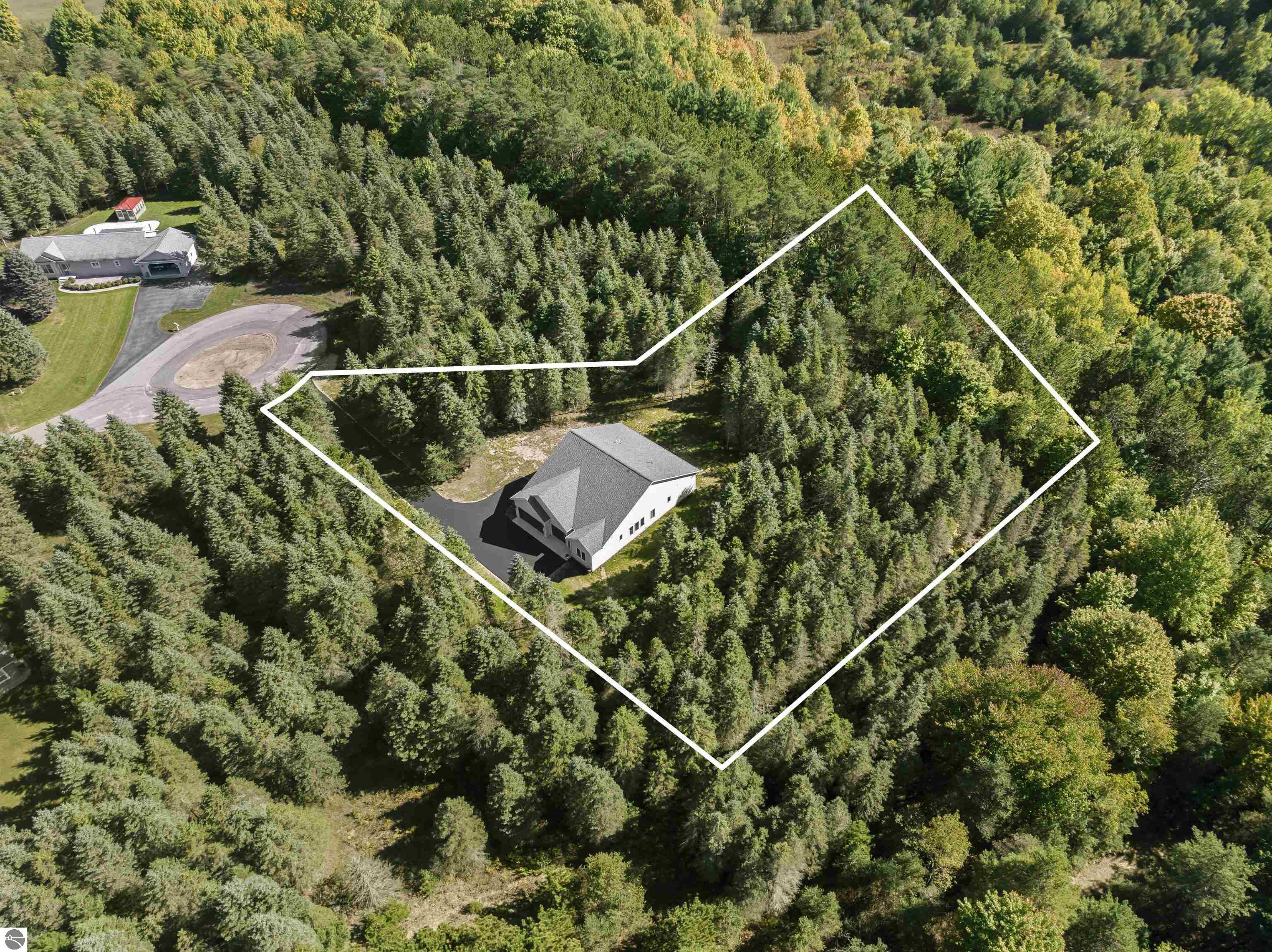 Aerial view of a house within a white-outlined wooded lot, surrounded by dense trees.