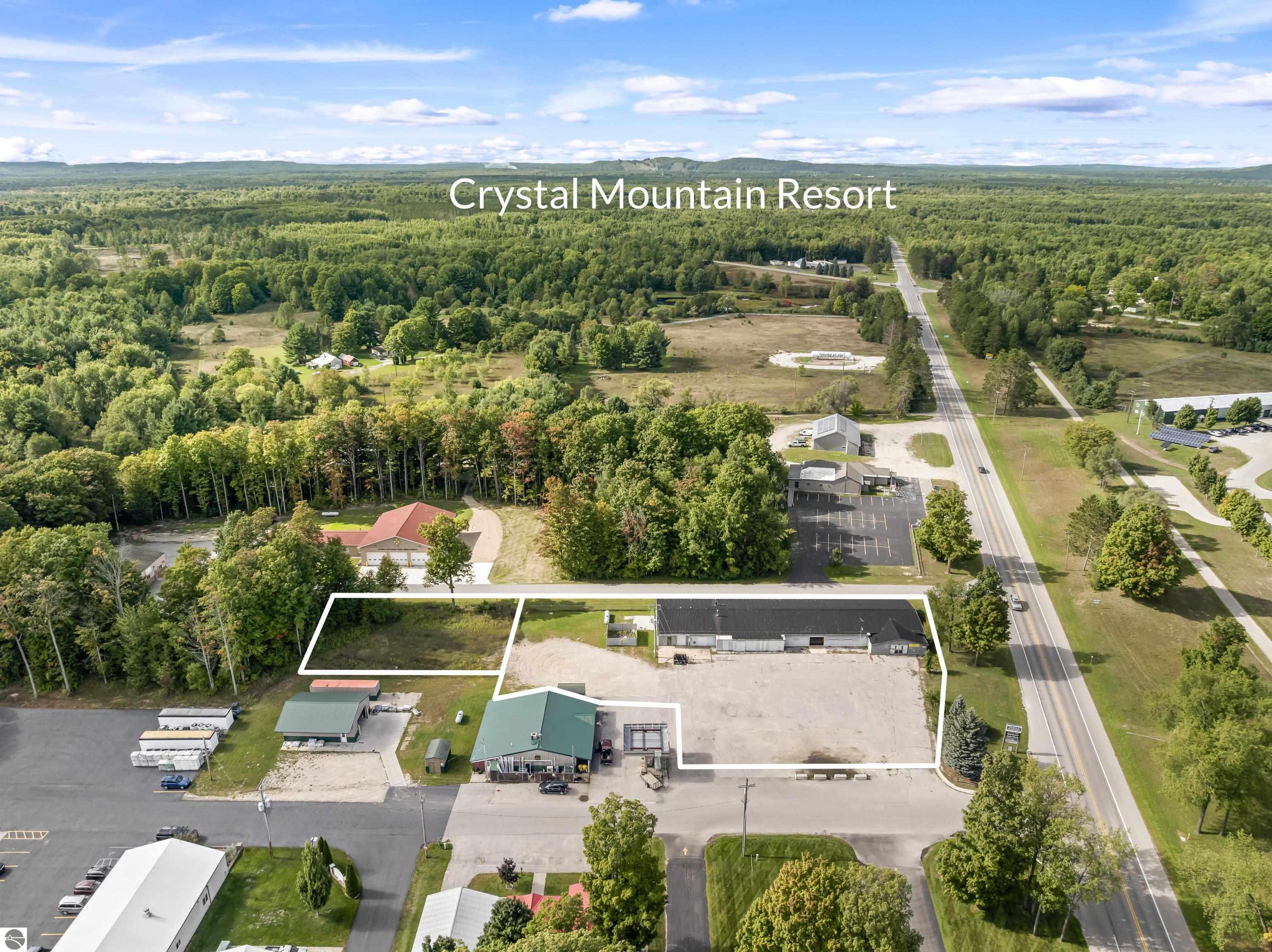 Aerial view of a commercial parcel outlined in white, with a long building beside a road and wooded countryside beyond.