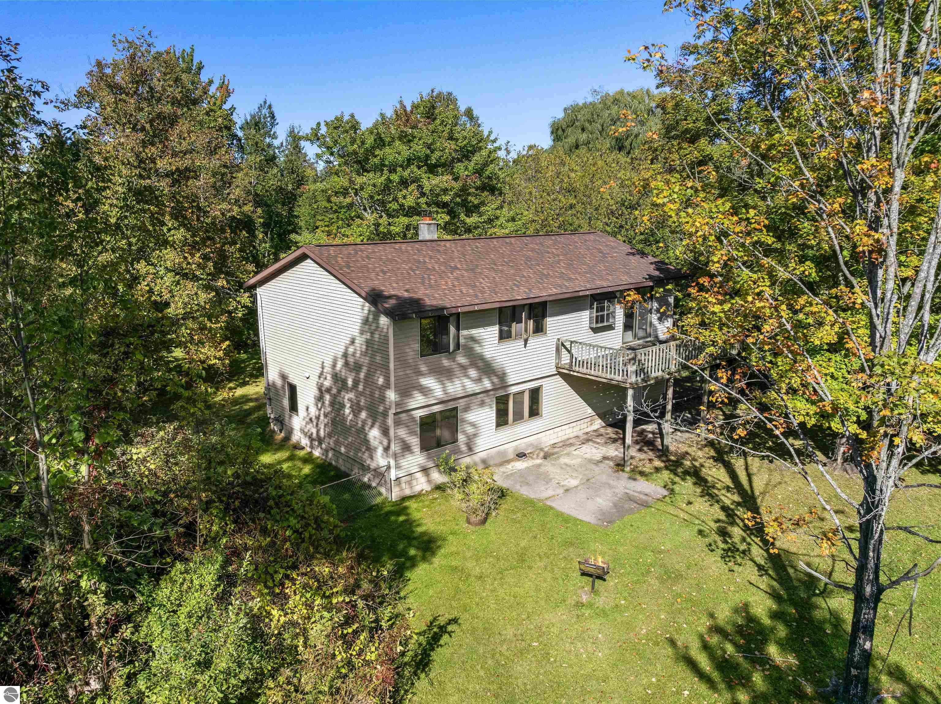 Two-story house with a raised deck, concrete patio, and wooded autumn yard.