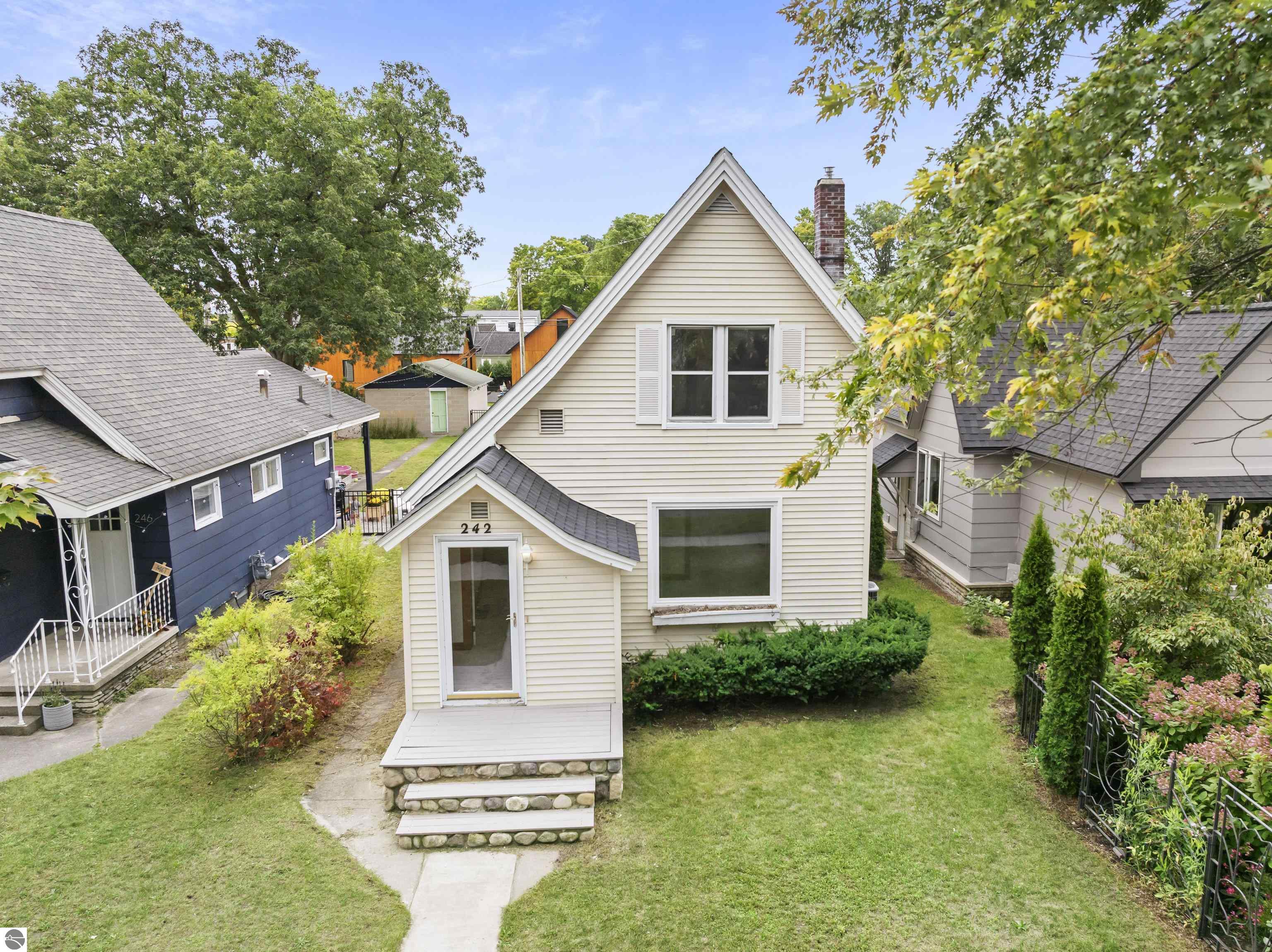 Cream gabled house numbered 242, with stone entry steps and neighboring homes close on either side.