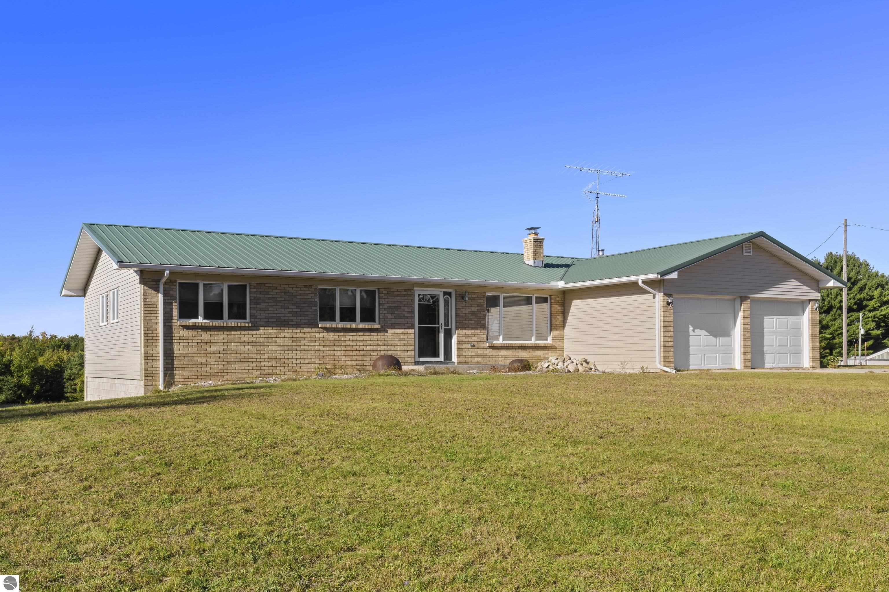 Single-story brick-and-siding house with a green metal roof, attached two-car garage, and broad lawn.