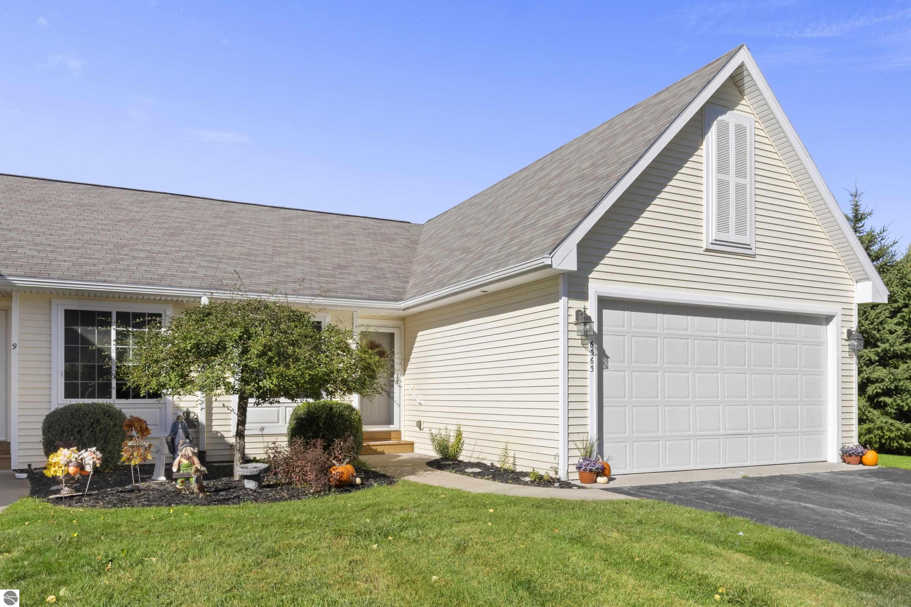 Light-sided home with a steep gable, two-car garage, and autumn decorations in the front garden.