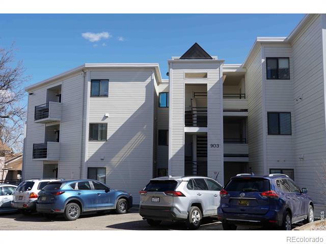 White multi-story residential building with balconies and parked cars in front.