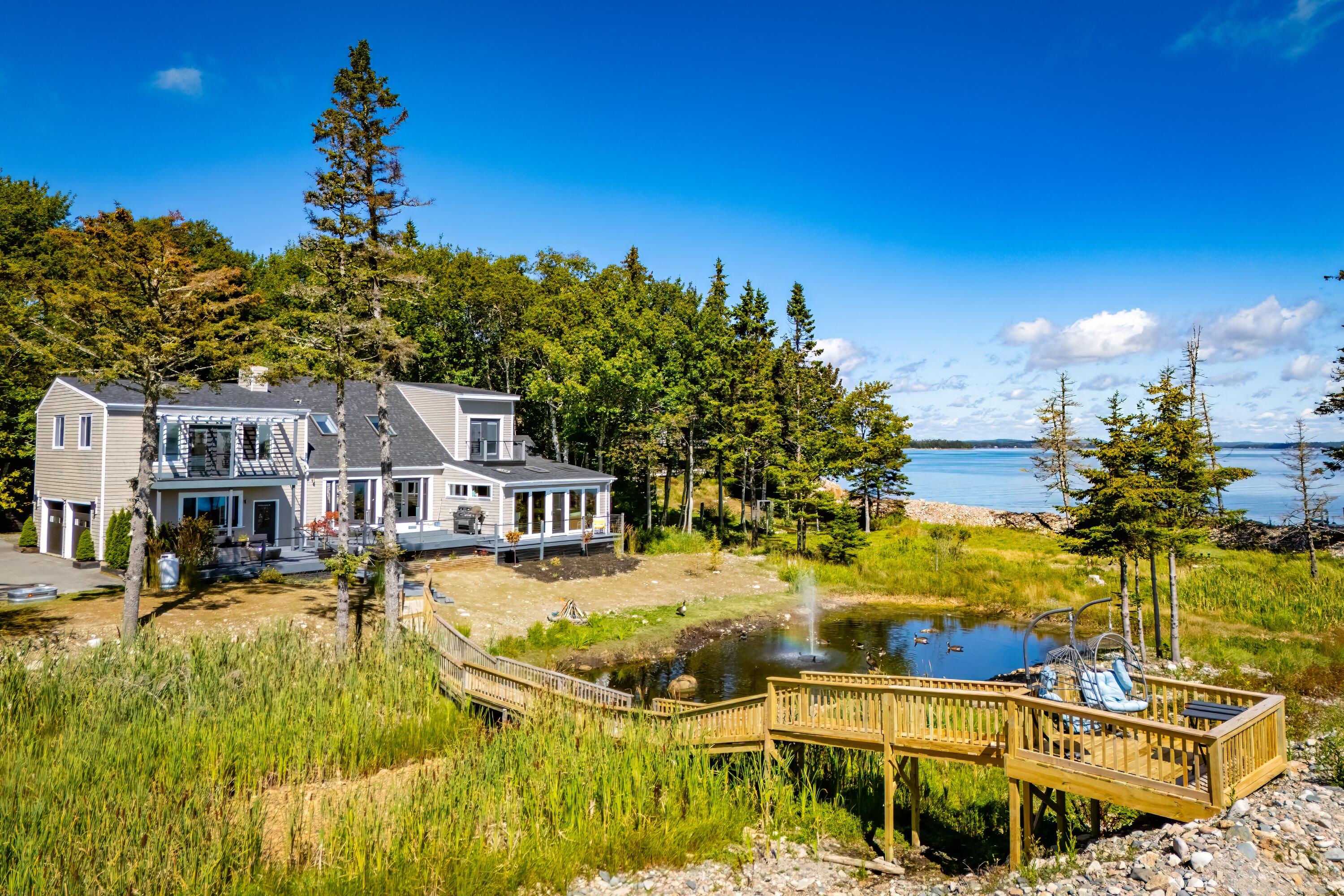 Coastal home beside the water, with a boardwalk over marsh grass and a deck surrounding a pond.