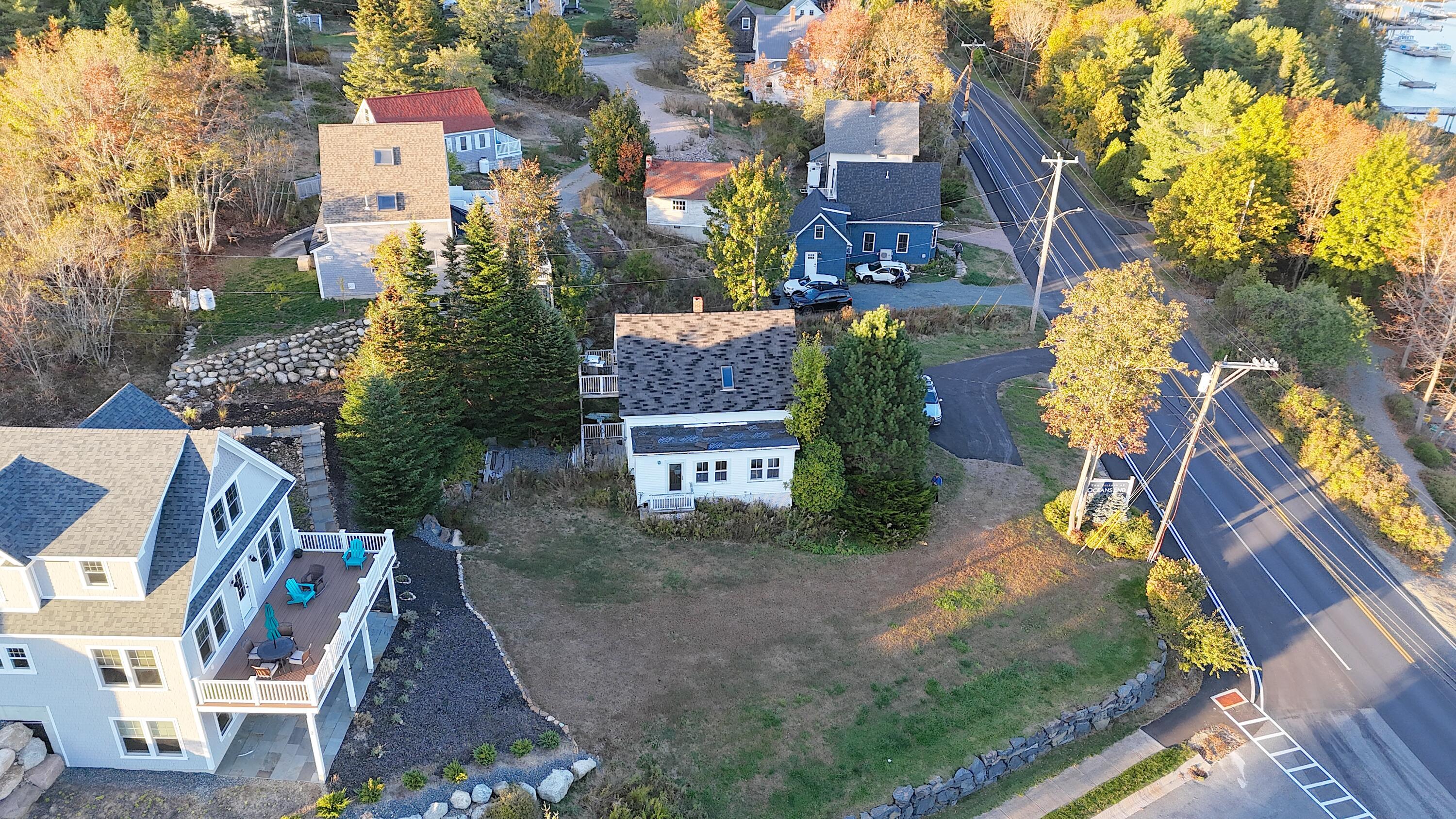 Aerial view of a white house on a grassy corner lot beside Main Street, with harbor water nearby.