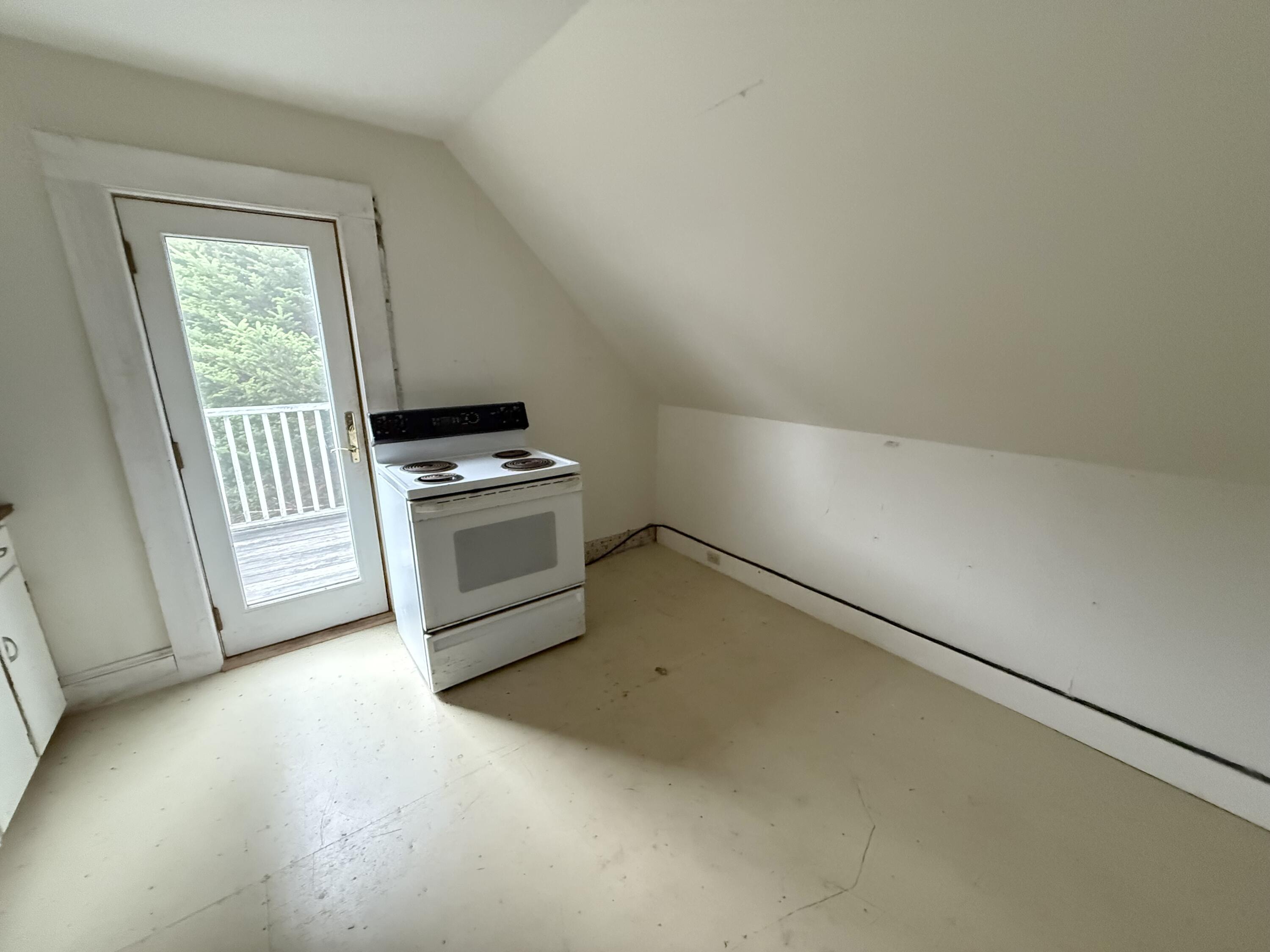 Vacant kitchen with an electric range beside a glass door opening onto a deck.
