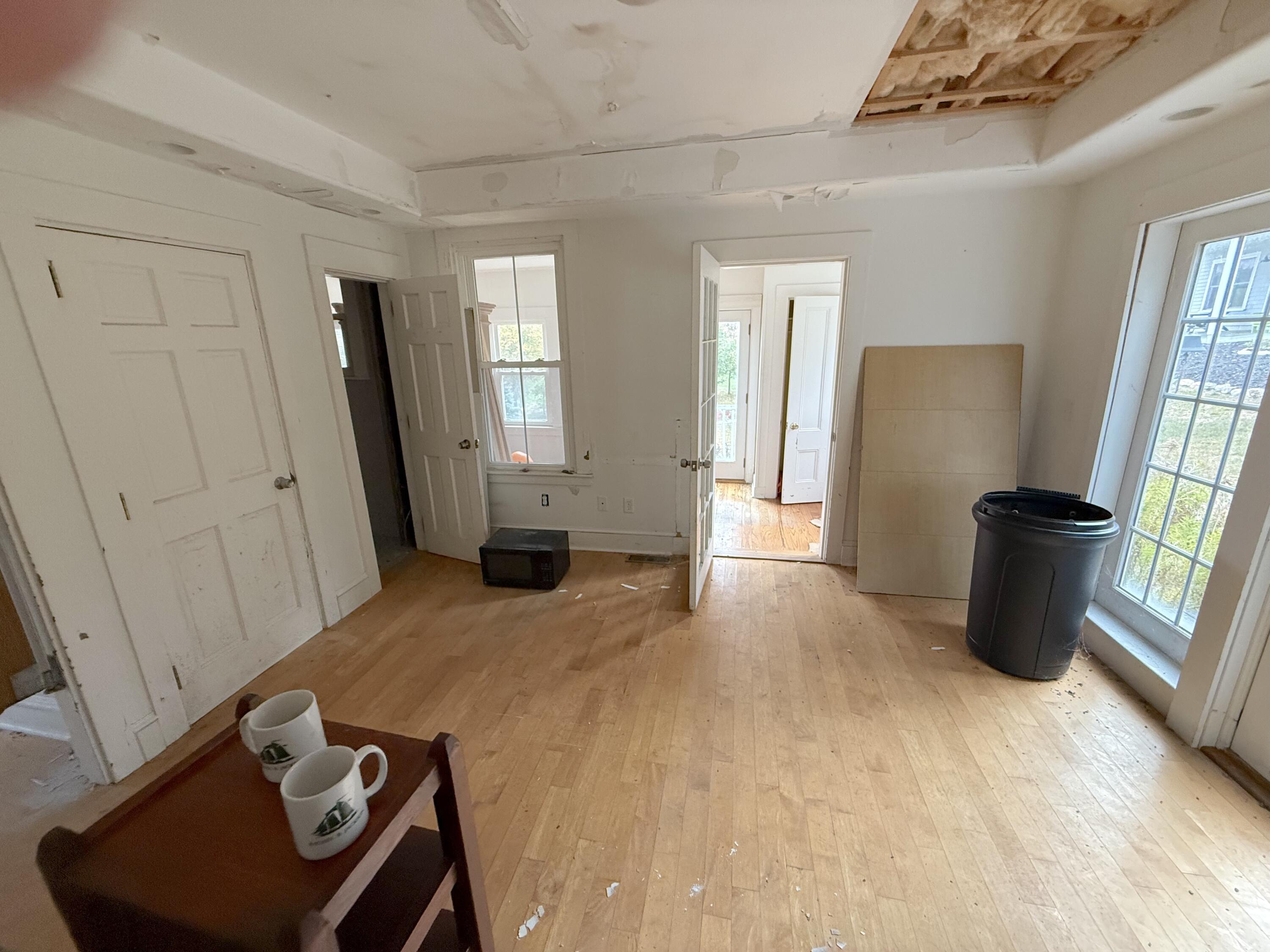 Room under construction with worn hardwood floors, tall windows, and an exposed section of ceiling.