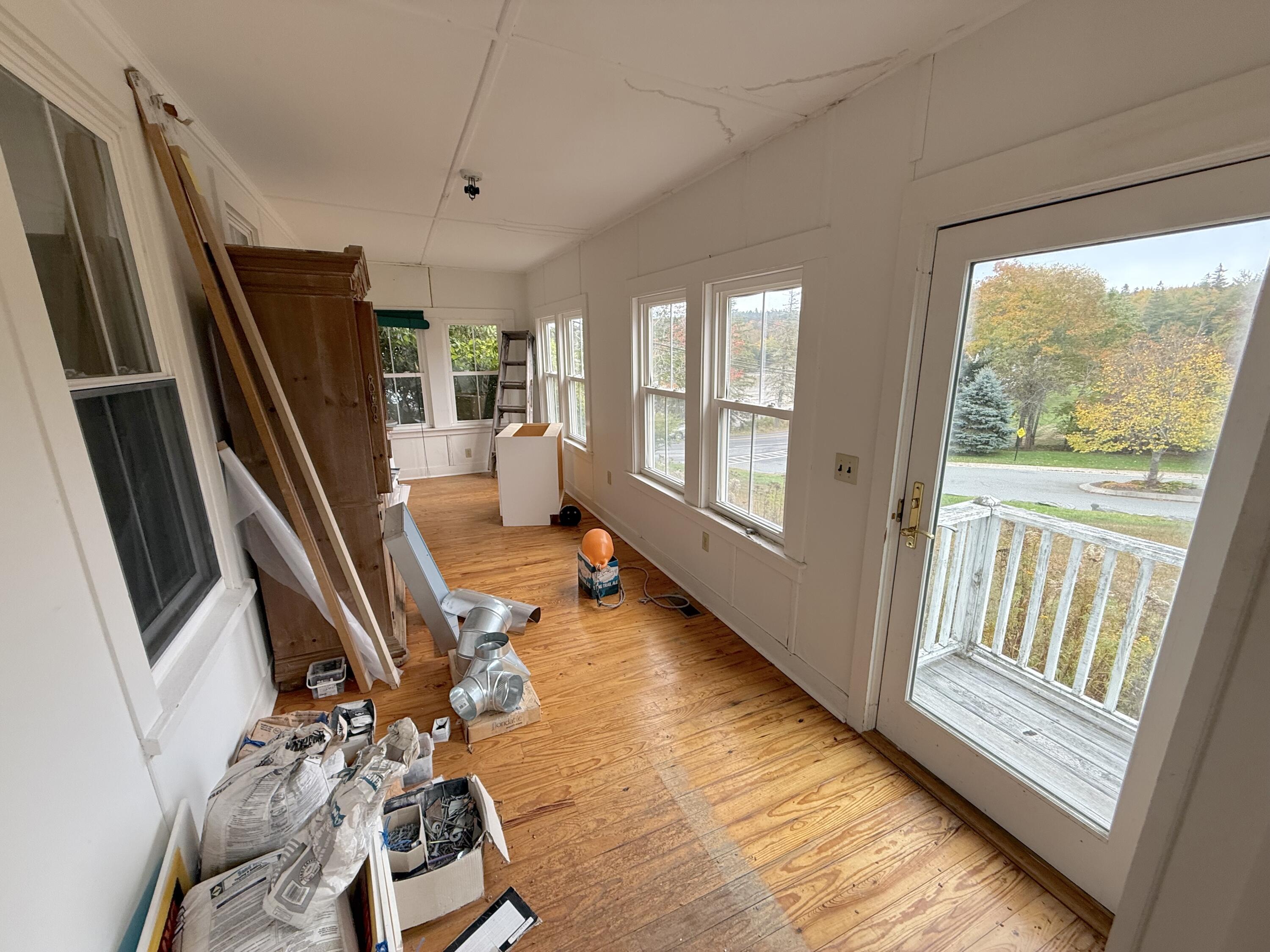 Long room with wood floors, renovation materials, multiple windows, and a glass door to a small porch.